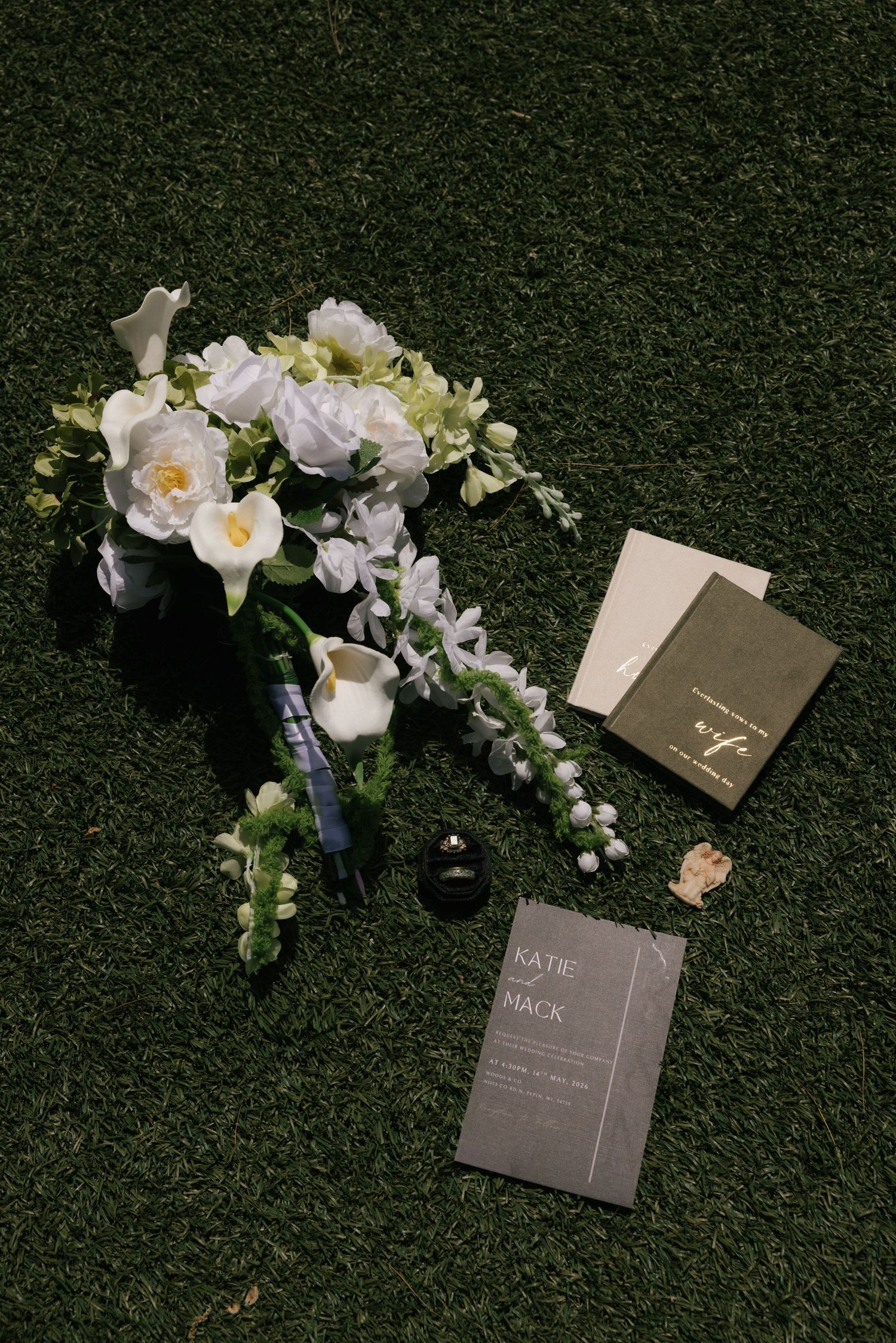 White floral wedding bouquet with invitation cards and ring box on green grass for Katie and Mack.