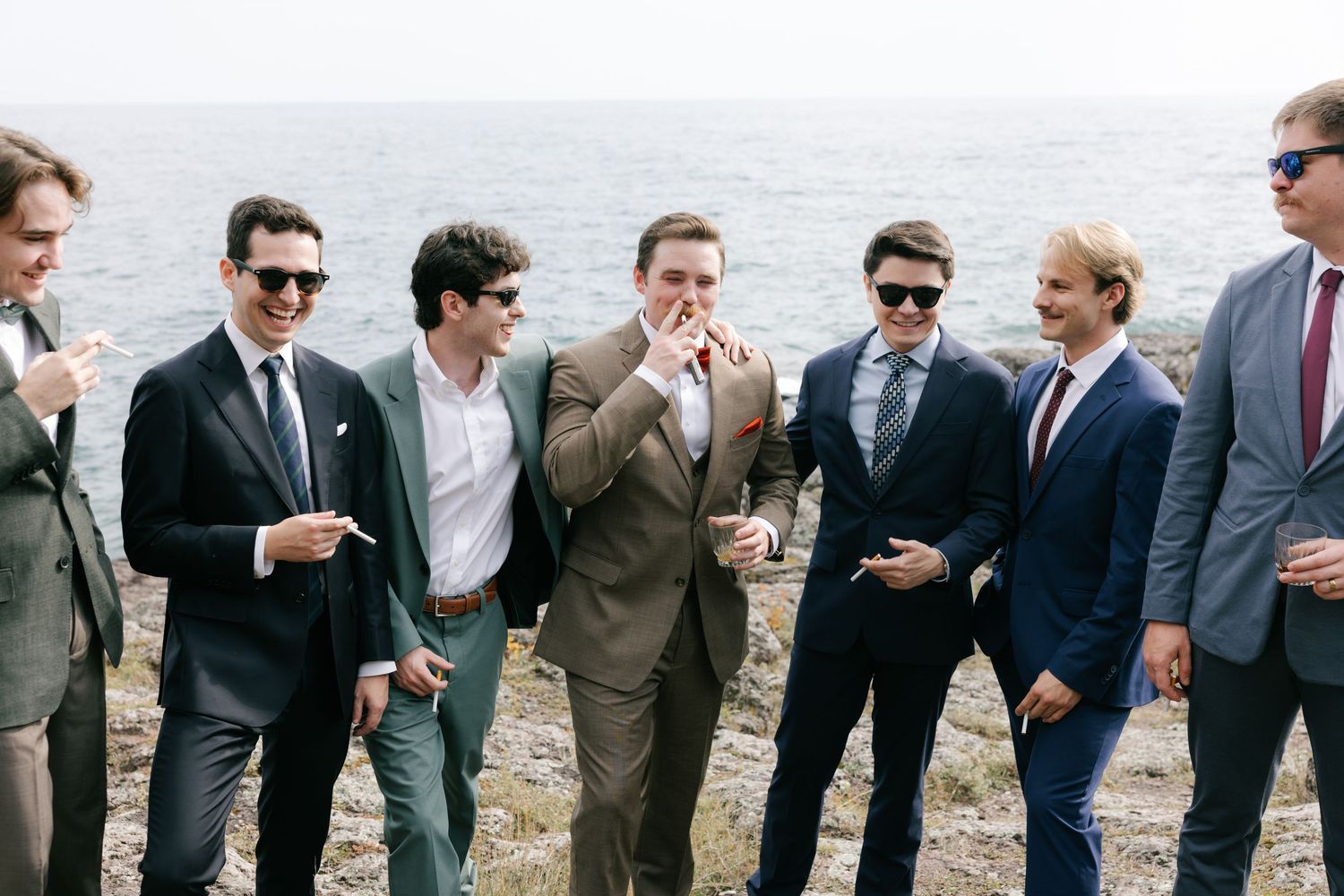 A group of well-dressed friends laugh together while standing outdoors near the ocean.