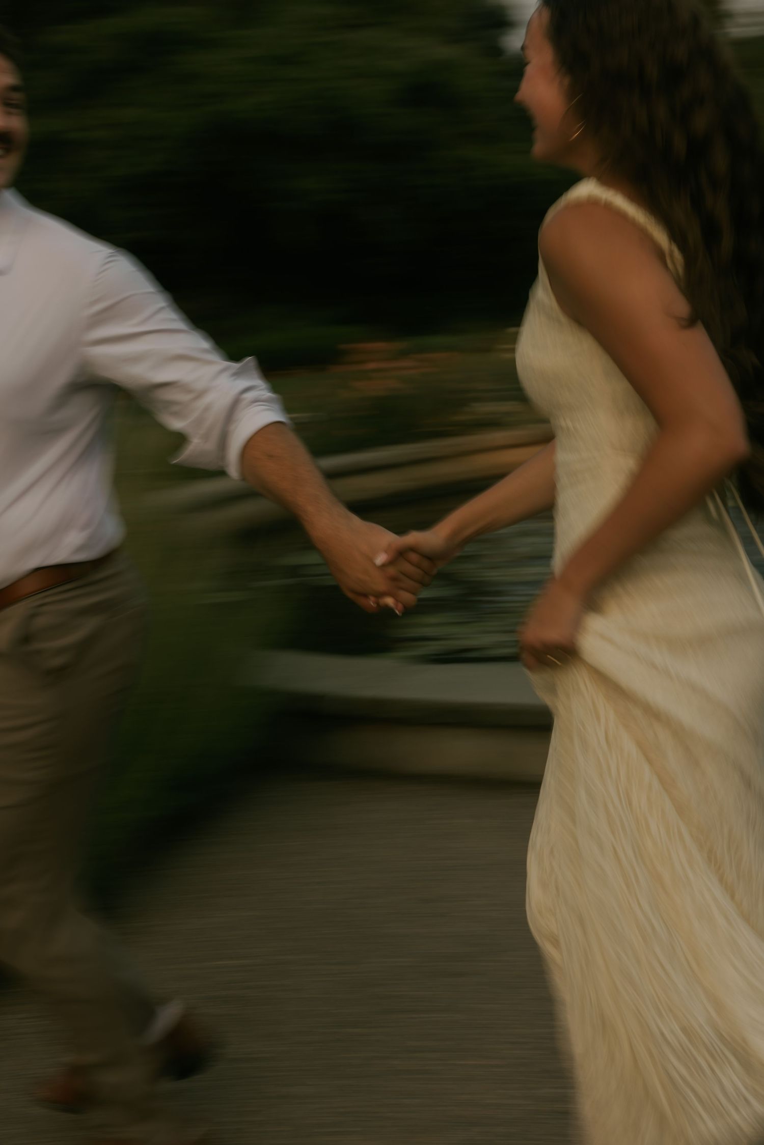 A blurred motion shot of a couple holding hands and running together, the woman in a flowing cream gown.