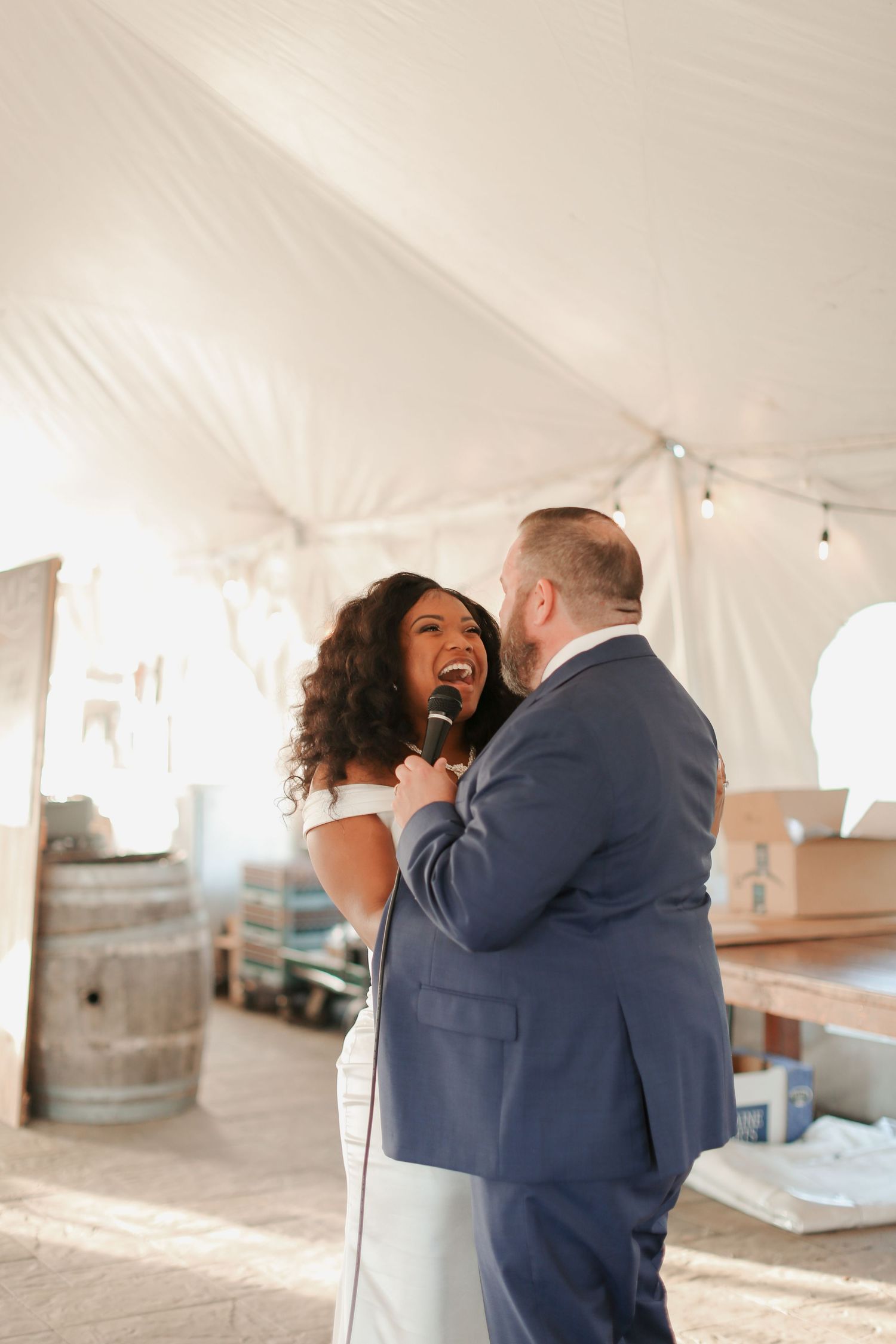 A couple laughs together while holding microphones during their wedding reception.