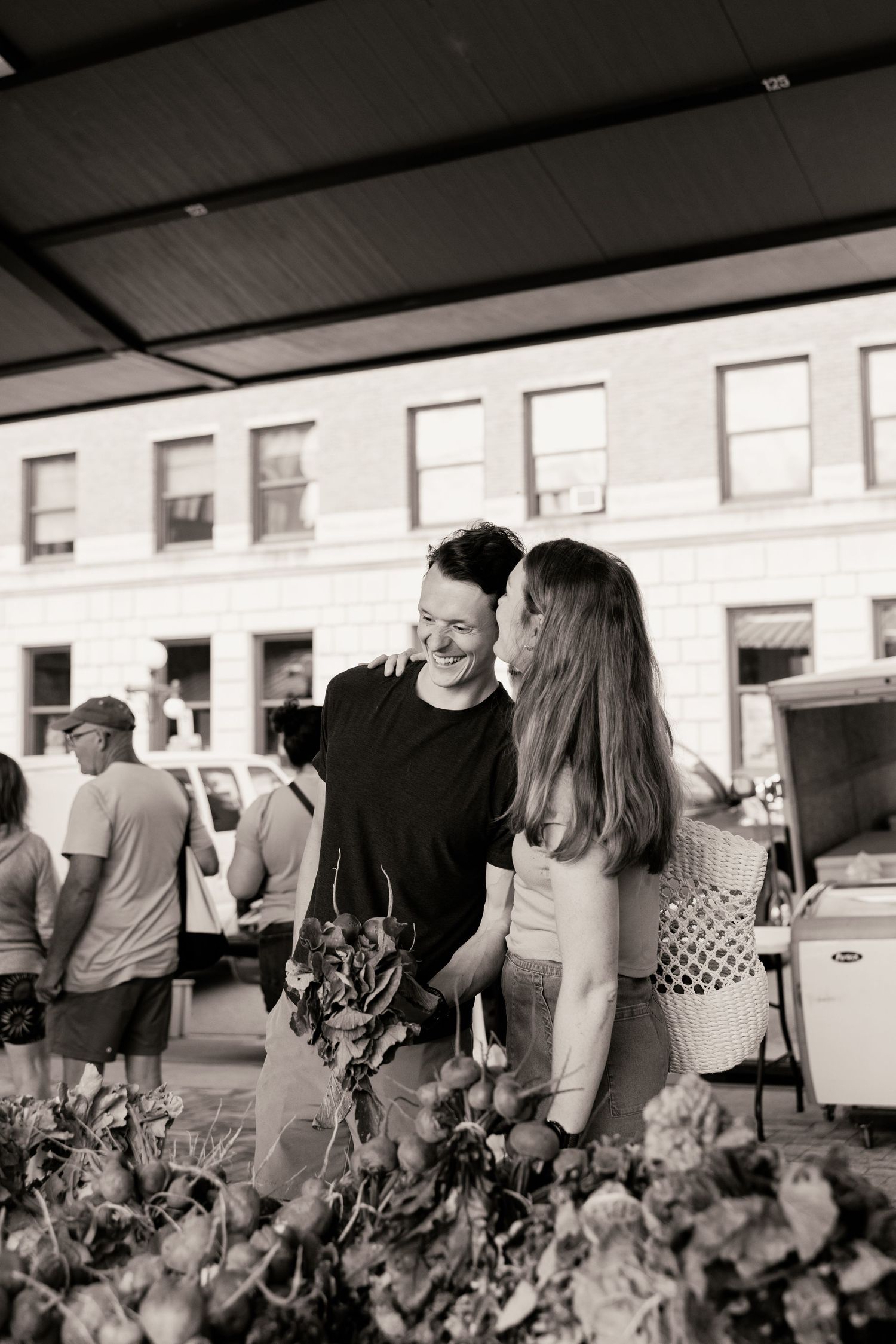 People gathered at an outdoor market or event space with flowers and stalls visible in black and white photography.