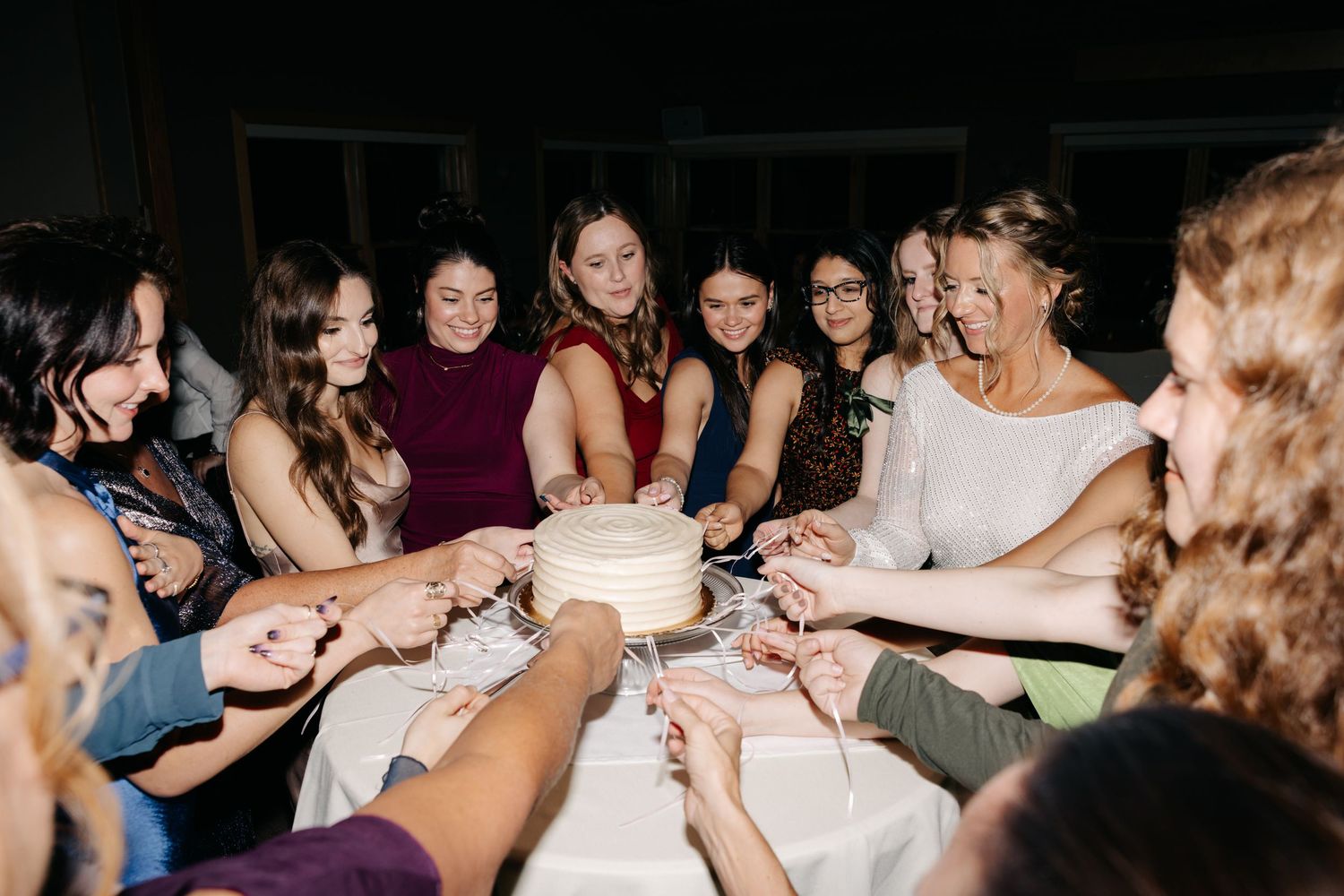 A group of friends gather around a table celebrating with cake at a nighttime party.