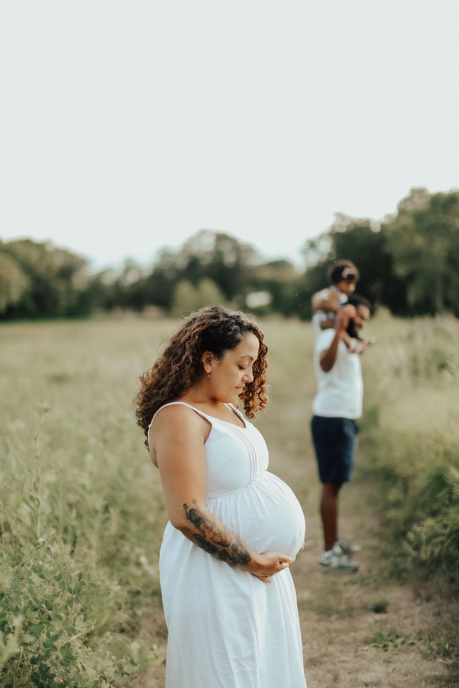 Maternity photoshoot in golden field during sunset with white flowy dress.