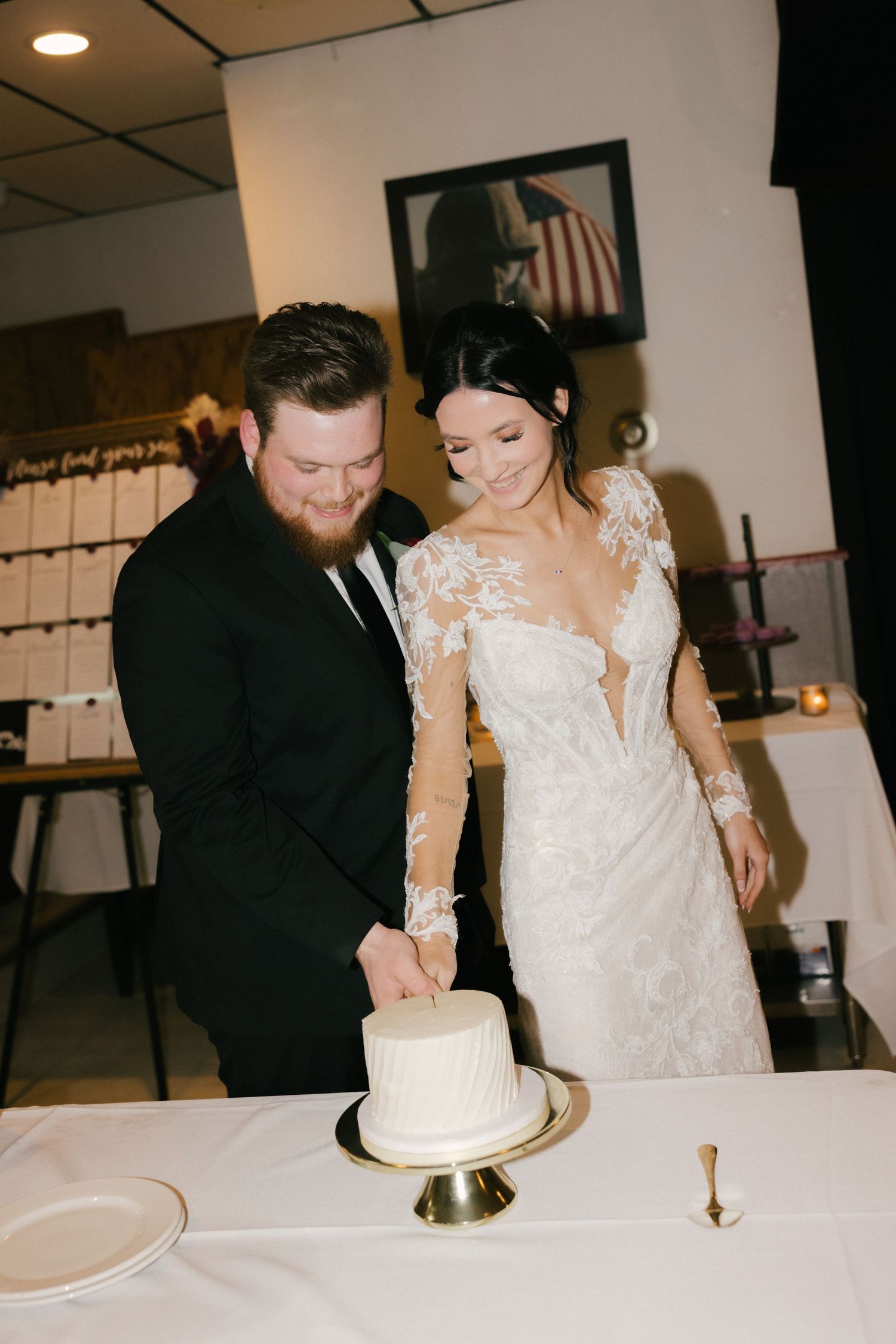 A couple in formal wedding attire cuts their elegant white wedding cake together at their reception.