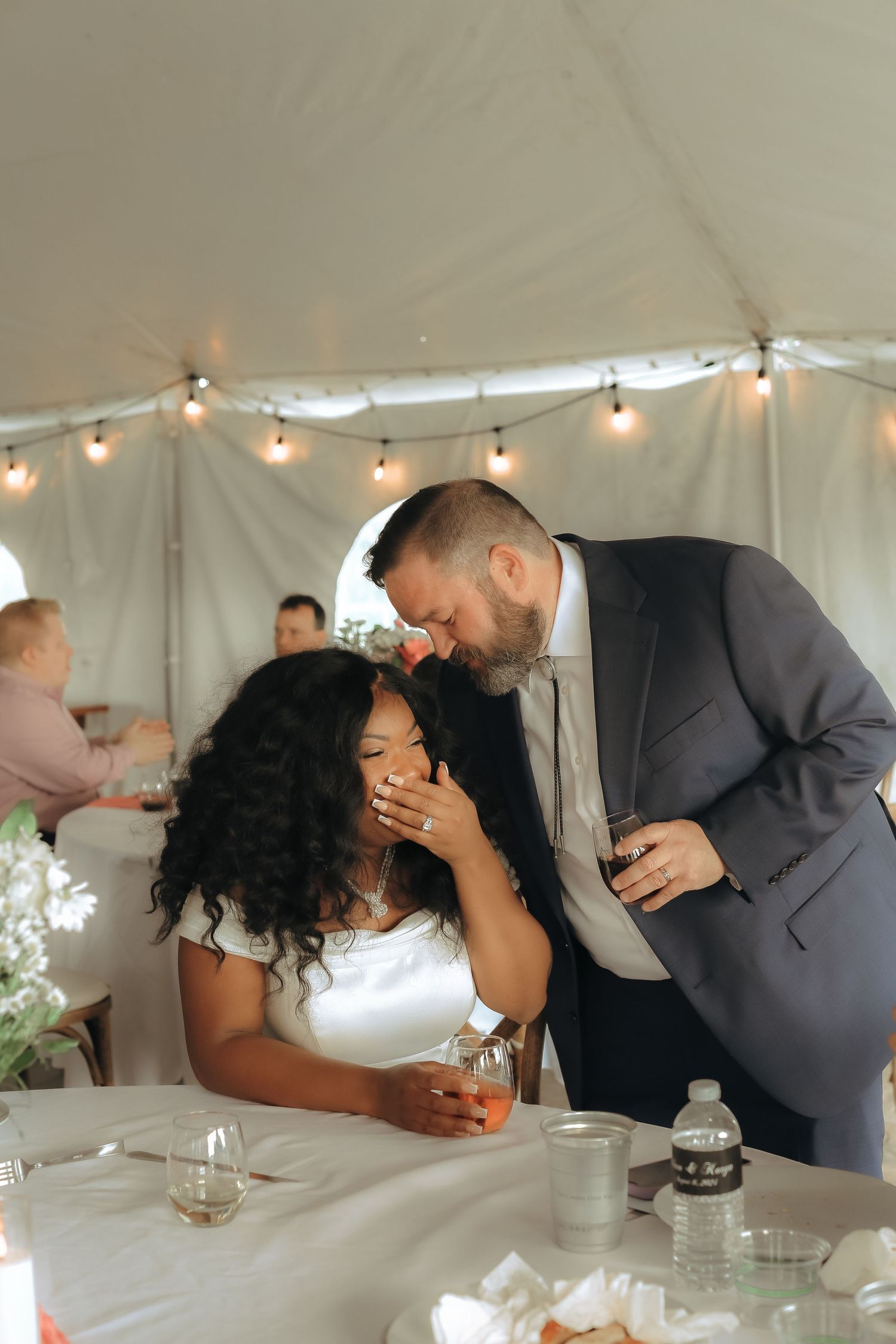A couple shares an intimate moment at their wedding reception under string lights.