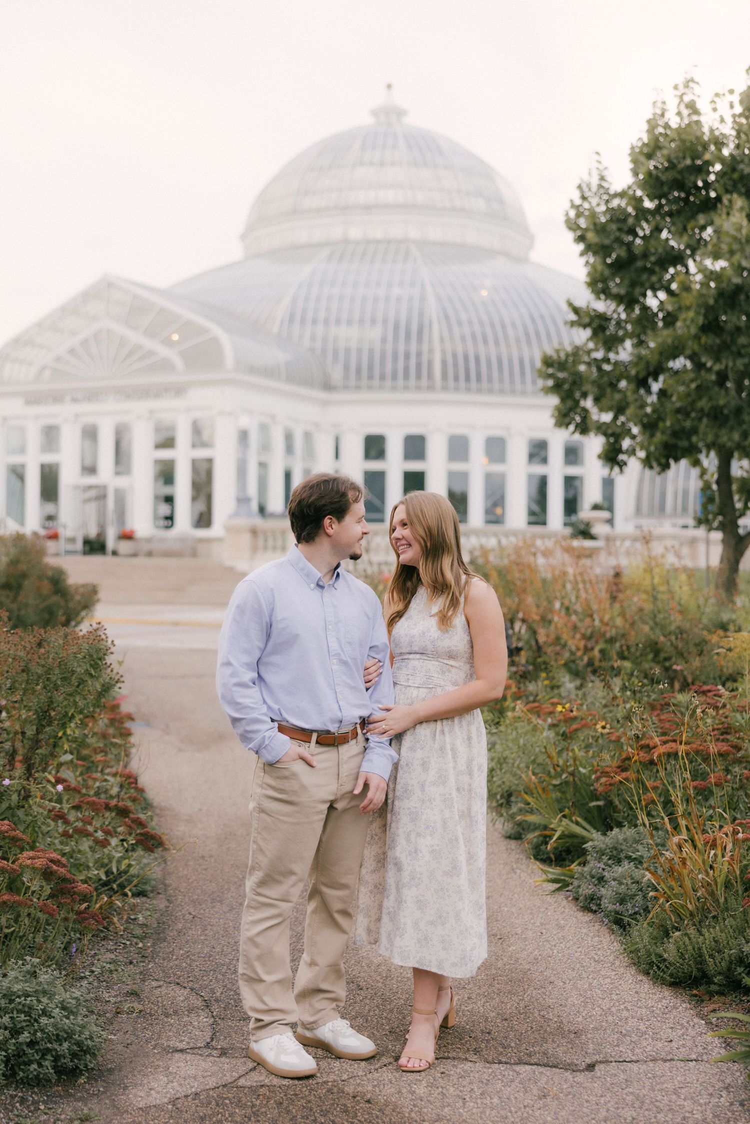 A couple shares a romantic moment in front of the Como Park Conservatory surrounded by blooming gardens.