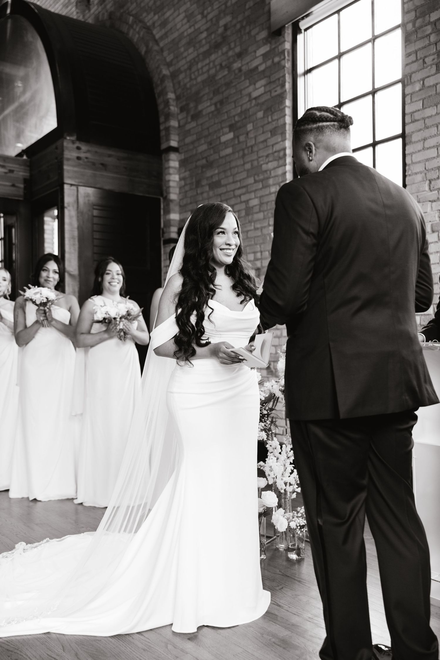 A series of black and white wedding photos showing tender moments in a brick-walled venue with large windows.