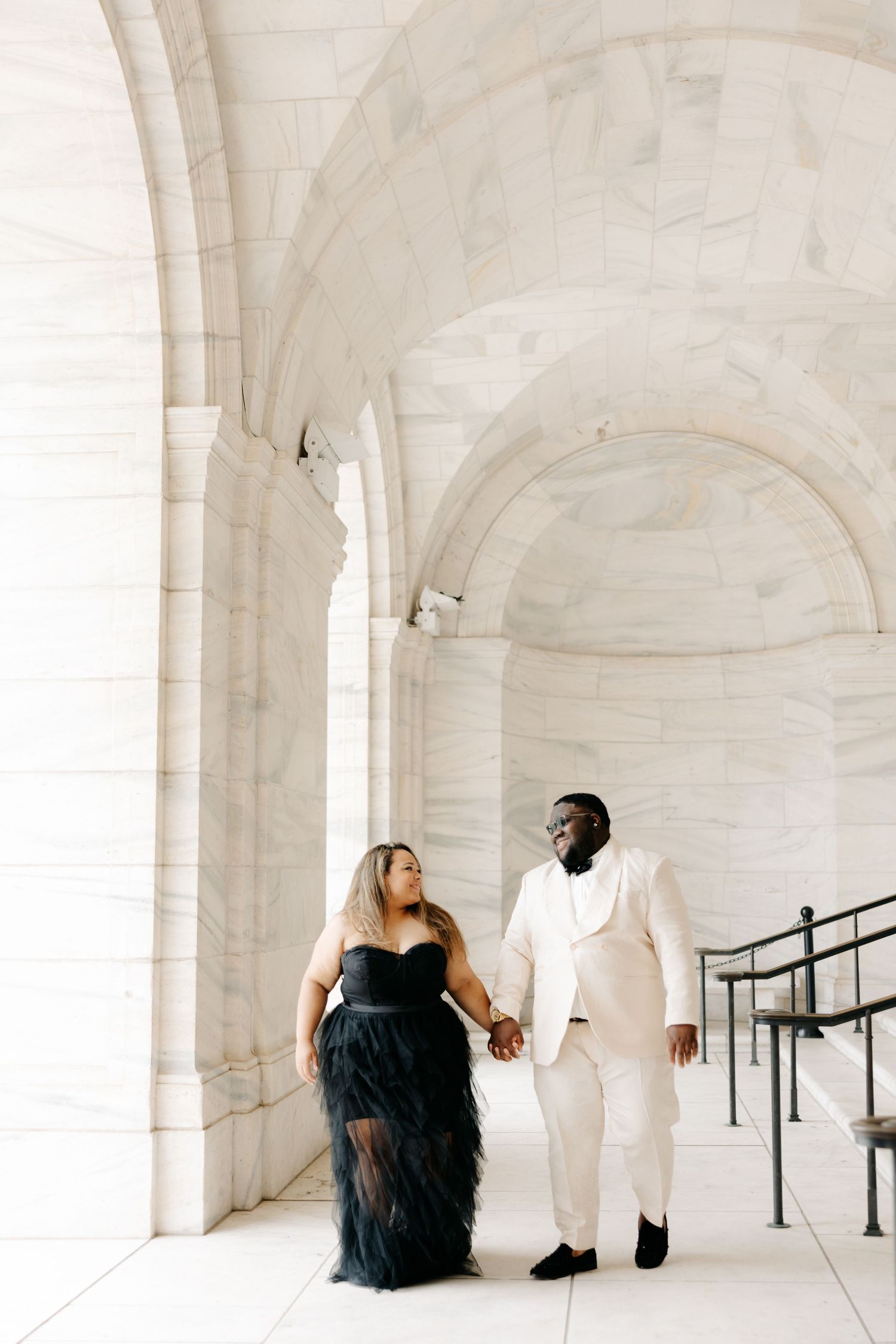 Artistic photo series showing couple in contrasting black and white outfits standing separated in white arched hallway.