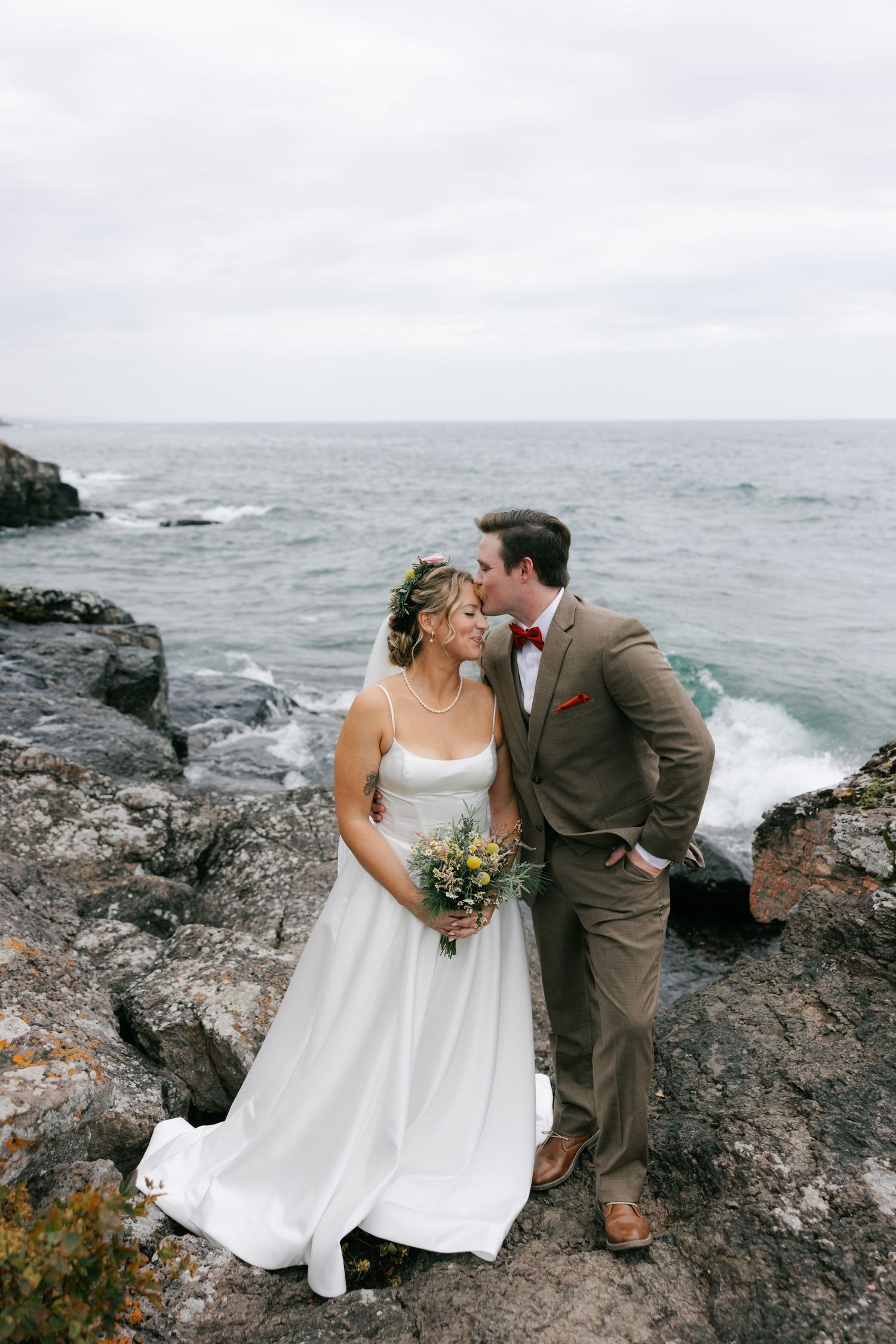 A couple shares an intimate moment on dramatic rocky cliffs overlooking a misty ocean coastline.
