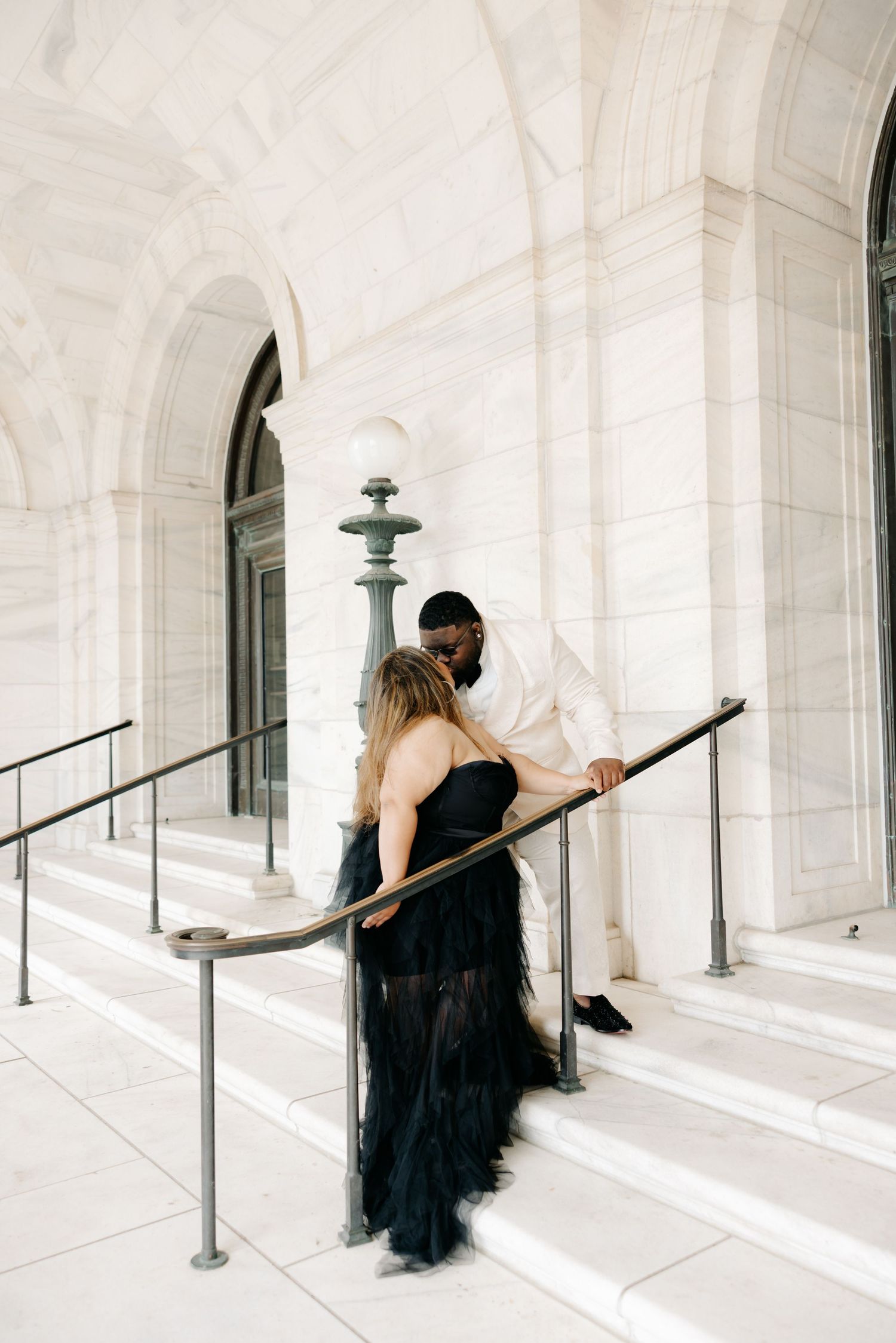 A figure in a black dress moves gracefully through a white marble colonnade creating an artistic contrast.
