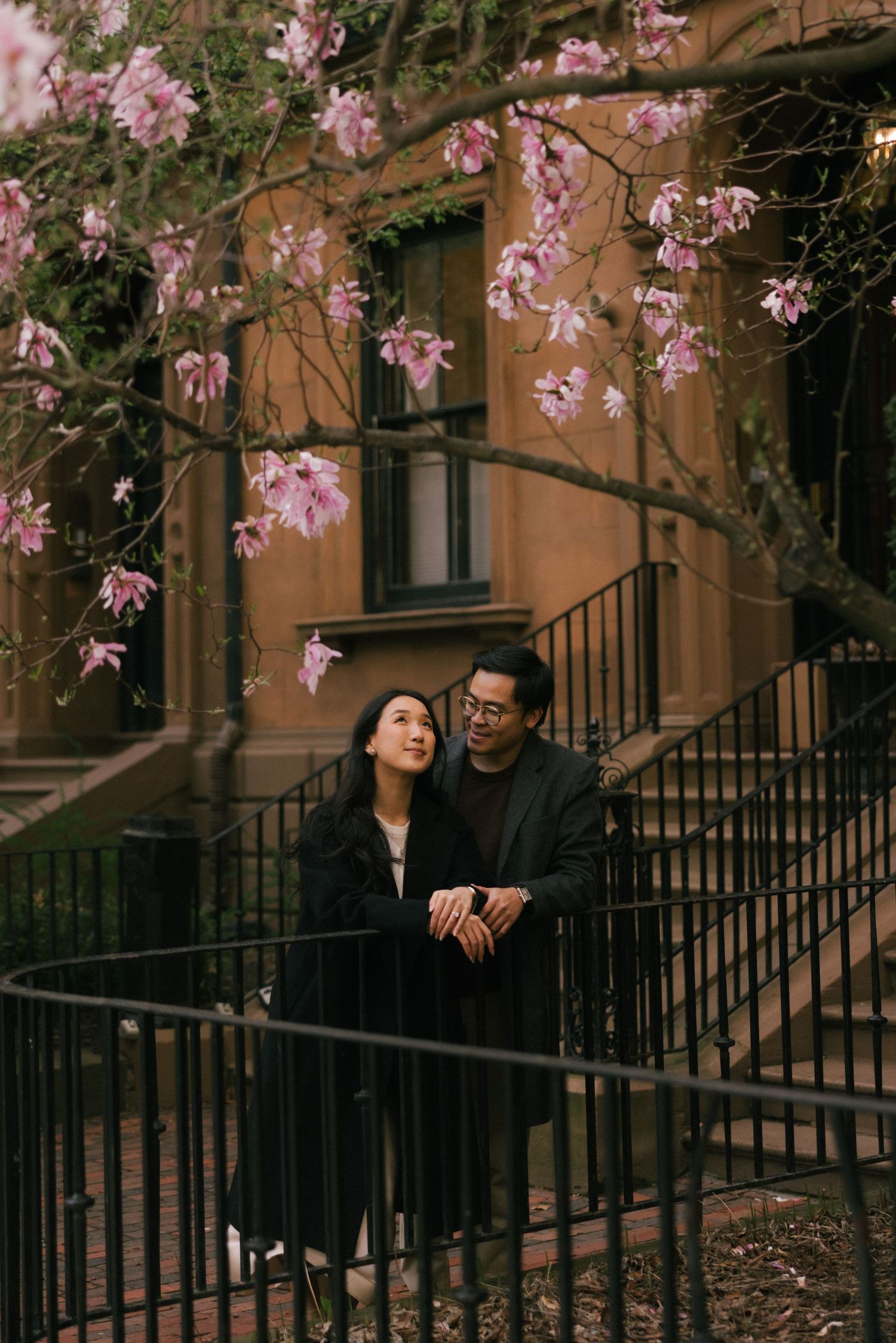 Couple embracing under pink magnolia blossoms on brownstone steps in spring.