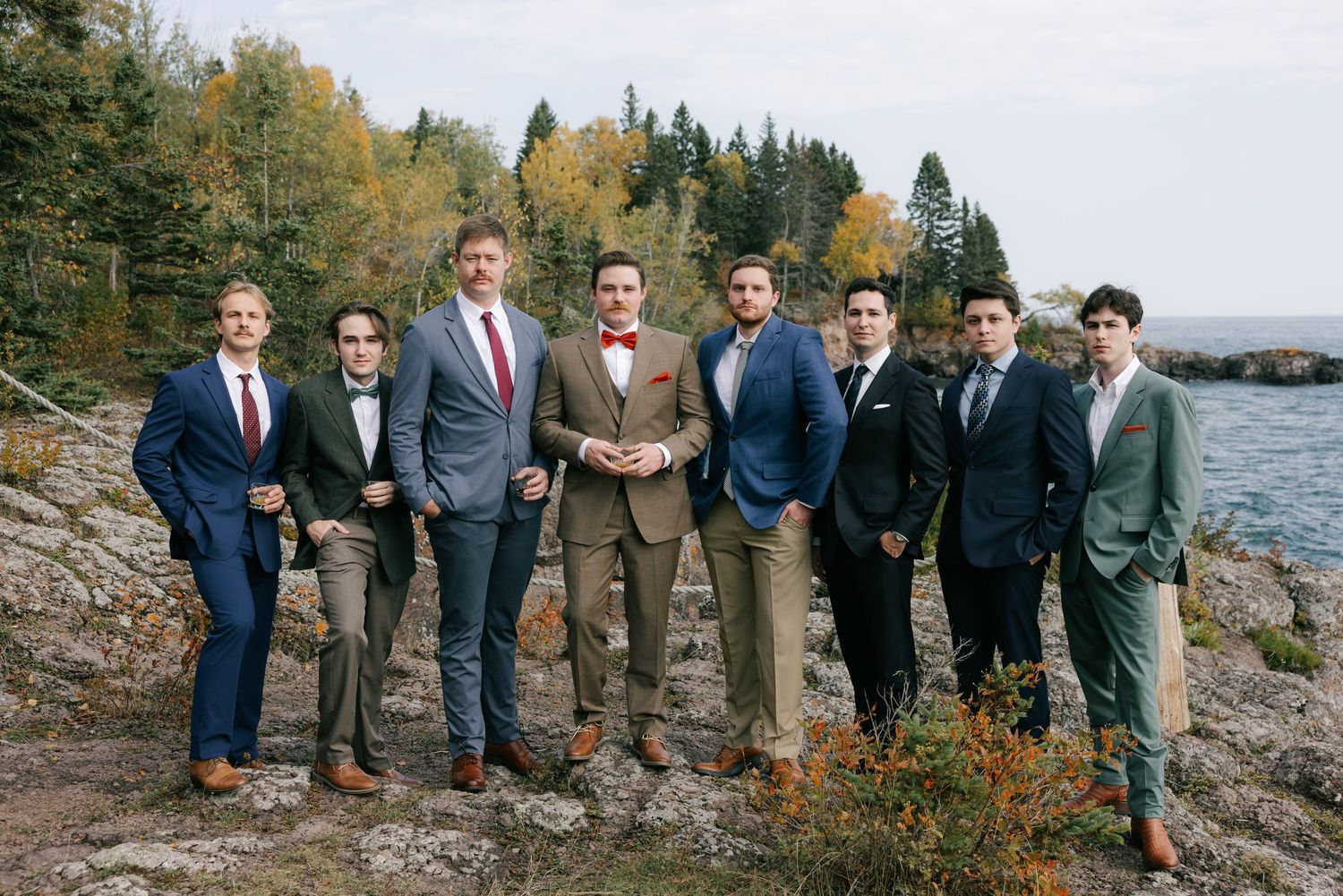 A group stands together on rocky coastal terrain surrounded by autumn foliage and evergreen trees.