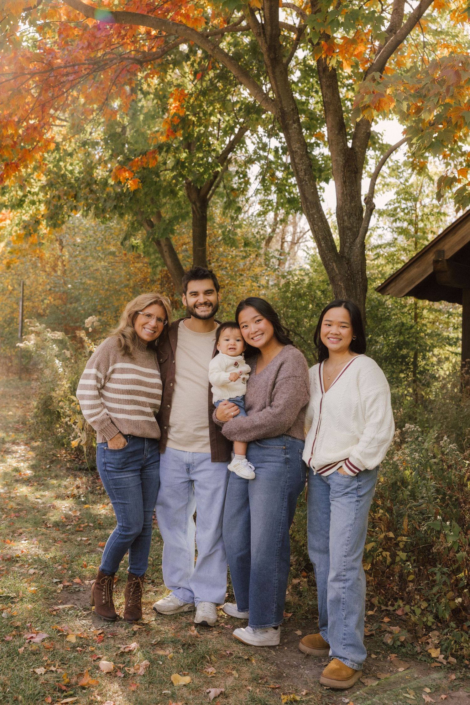 A group stands together against autumn trees with golden leaves in a casual outdoor photo session.