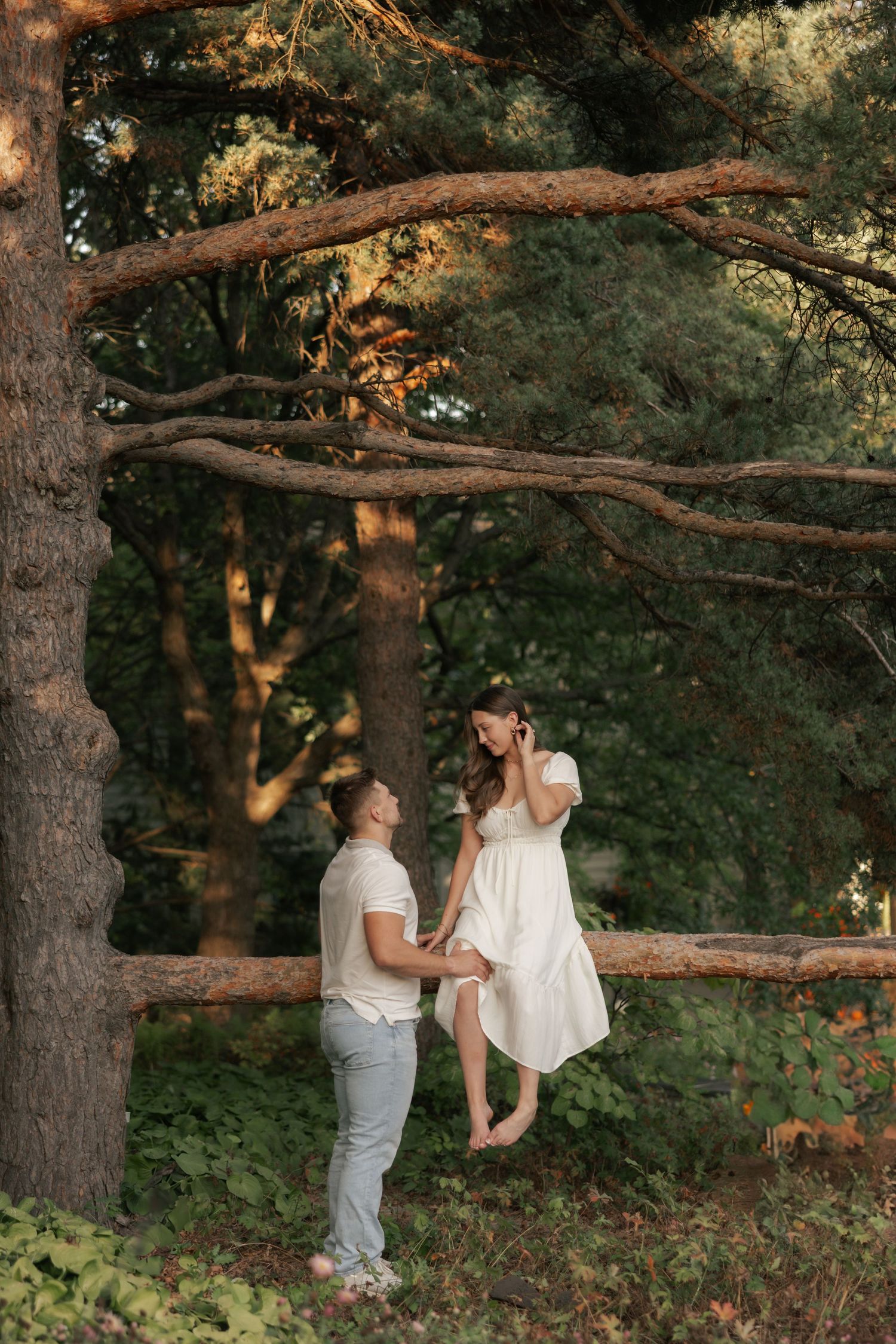 Two people share an intimate moment together in a wooded outdoor setting at sunset.