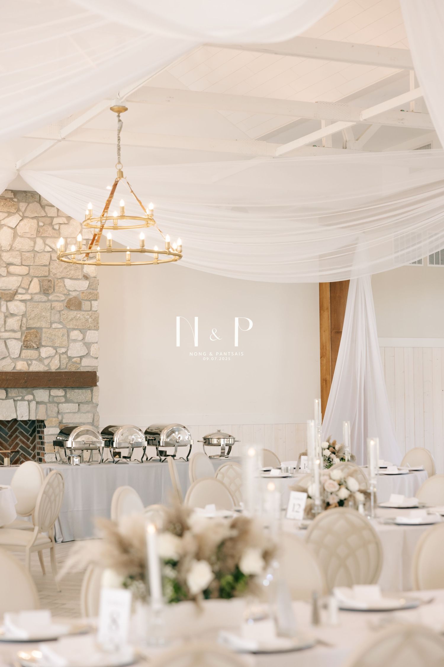 Elegant white wedding reception venue with stone walls, crystal chandeliers, and soft neutral table settings.