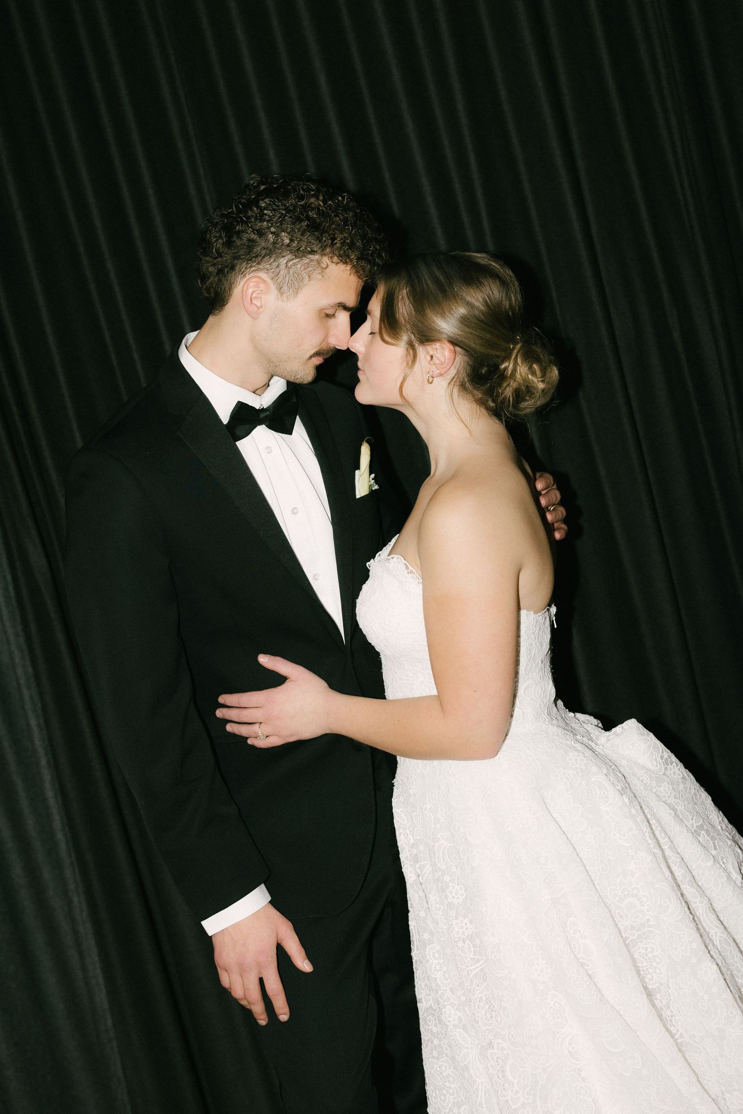 A romantic moment between newlyweds in formal wedding attire silhouetted against a dark background.