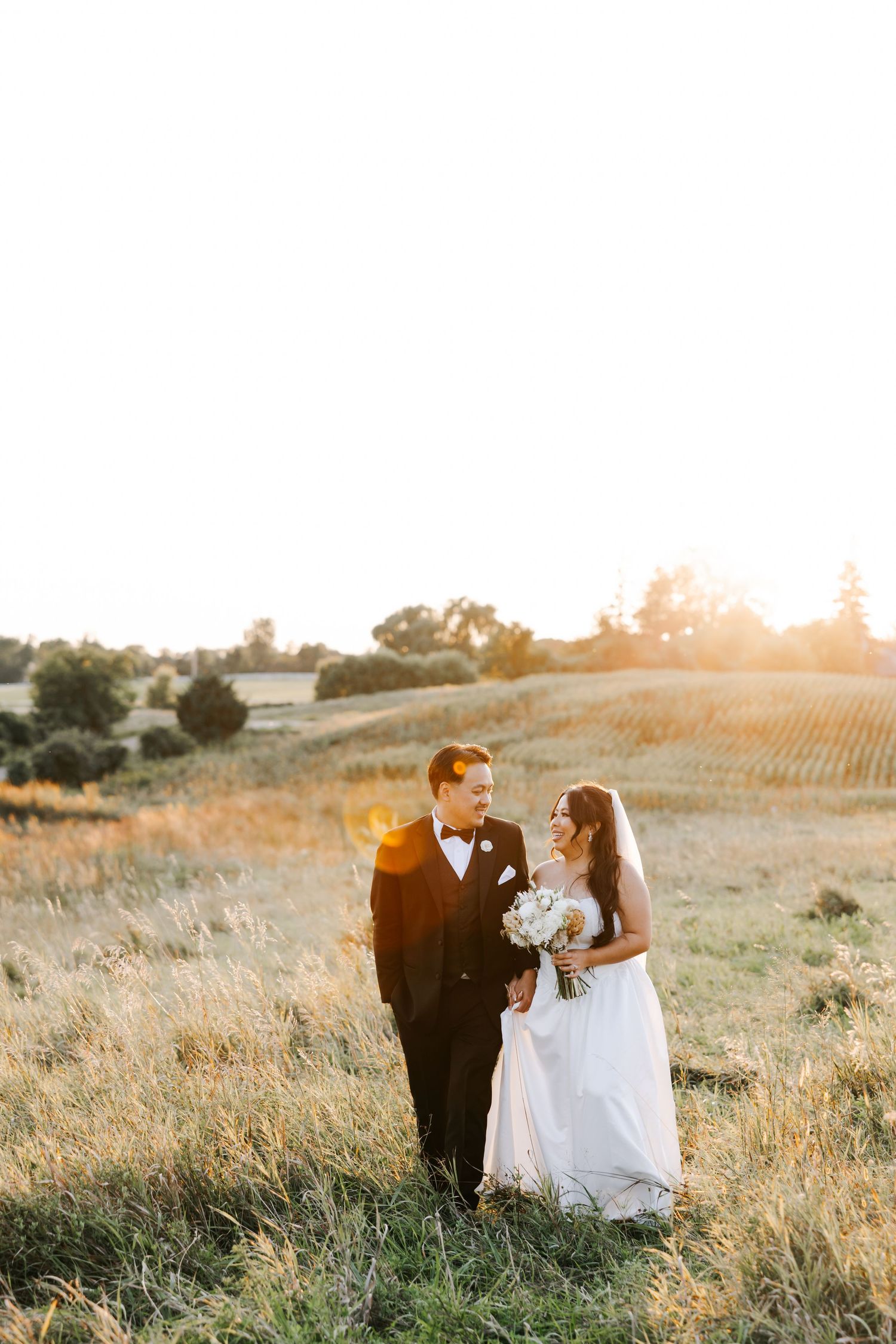 Newlywed couple sits together in a golden sunlit meadow during sunset photography session.