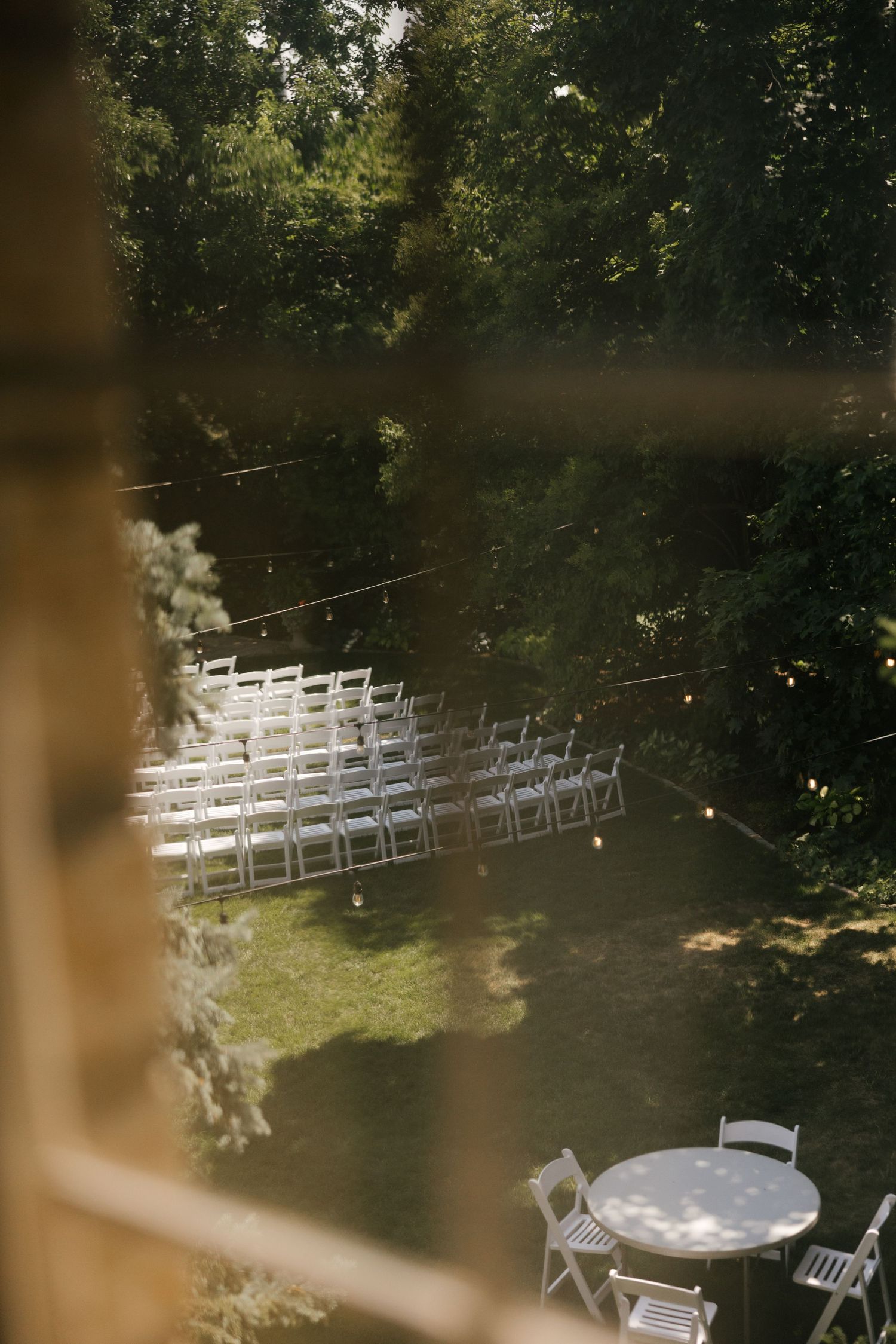 Aerial view of outdoor wedding ceremony setup with white chairs on green lawn surrounded by lush trees.