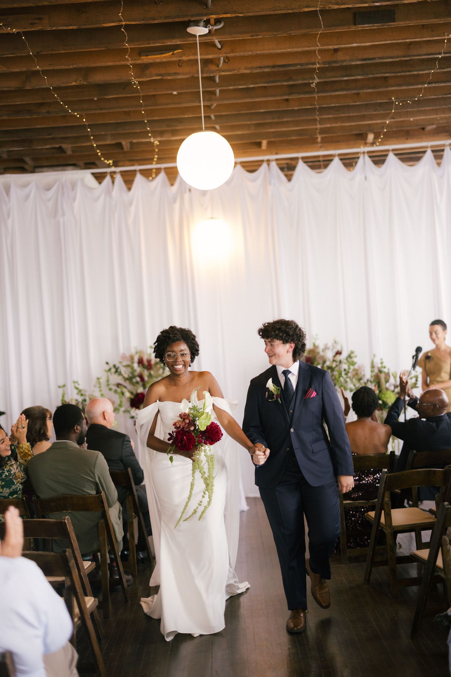 Bride and groom walk down the aisle hand in hand after wedding ceremony in elegant indoor venue.