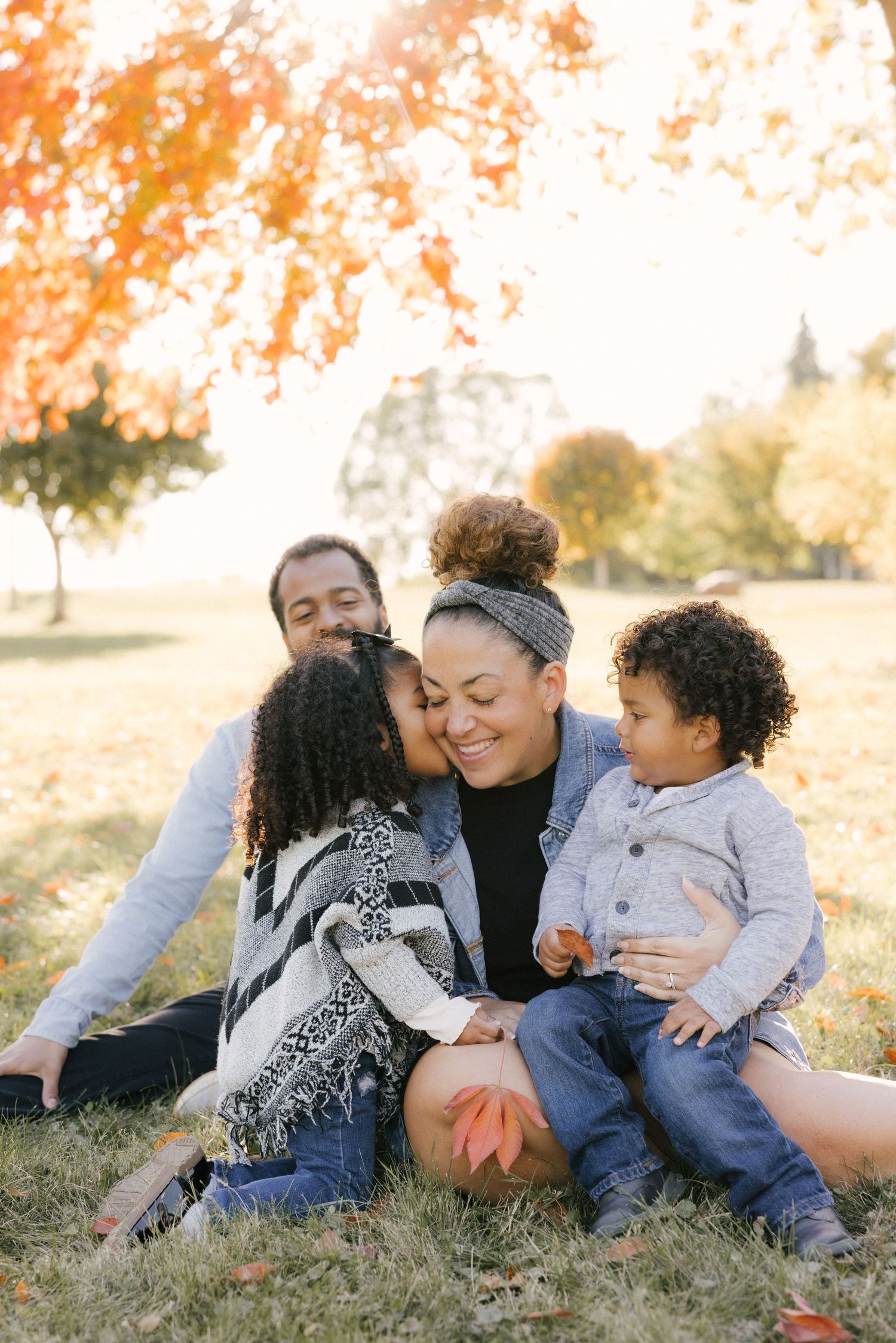 A family lying together on autumn grass sharing tender moments during an outdoor photo session.
