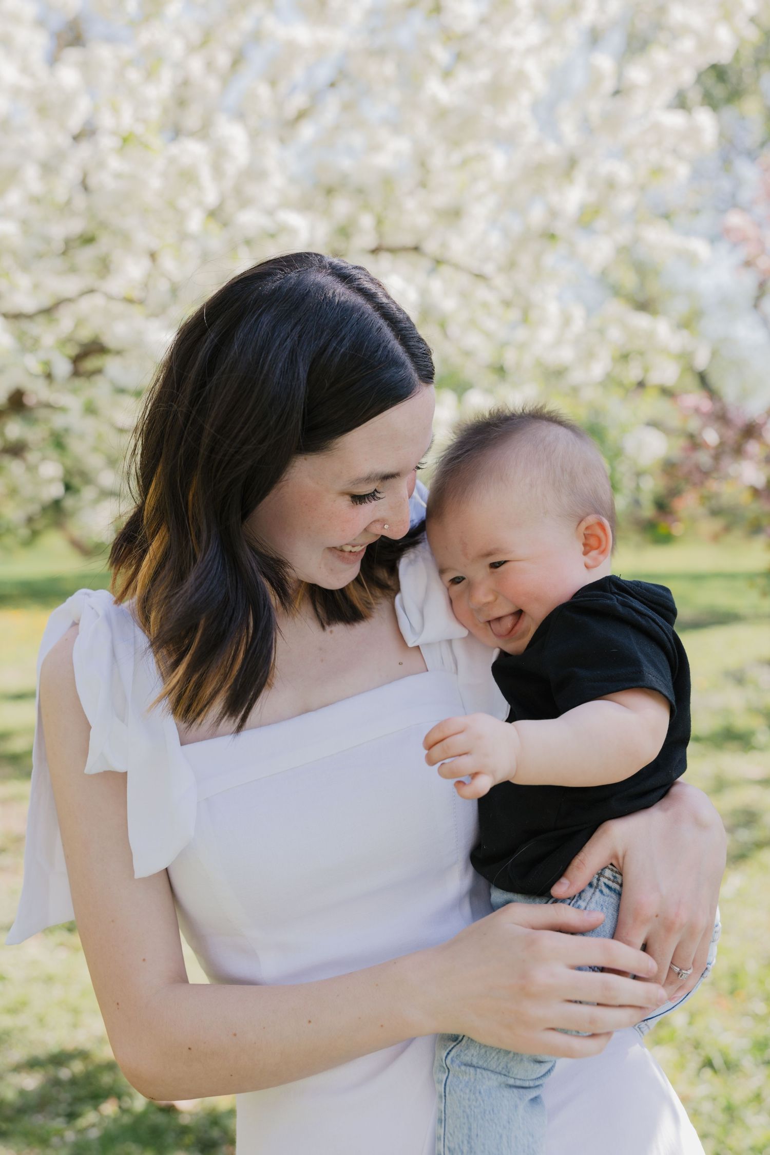A joyful moment captured between parent and baby laughing together under blooming spring trees.