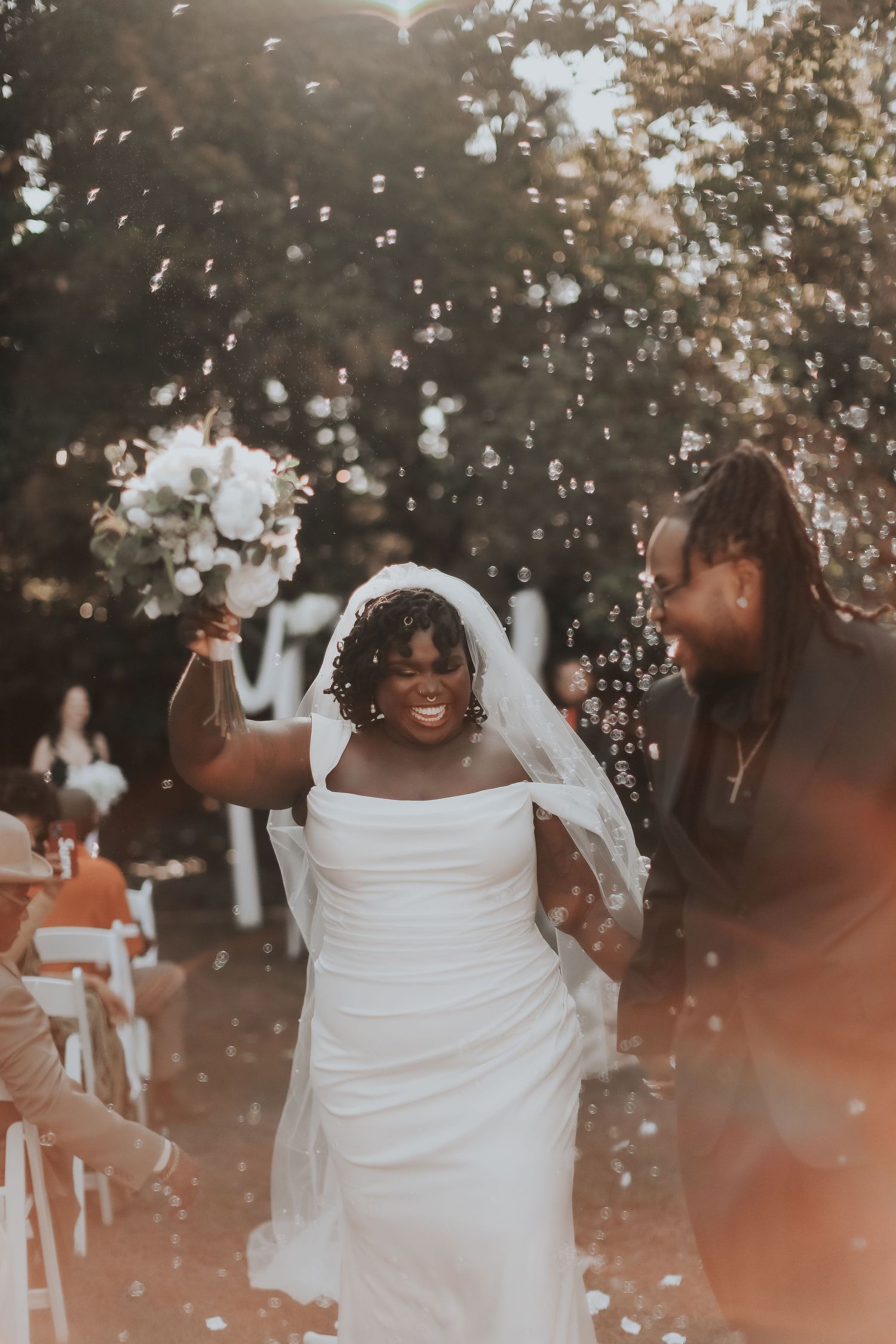 A joyful bride in a white dress holds a bouquet while surrounded by floating confetti.