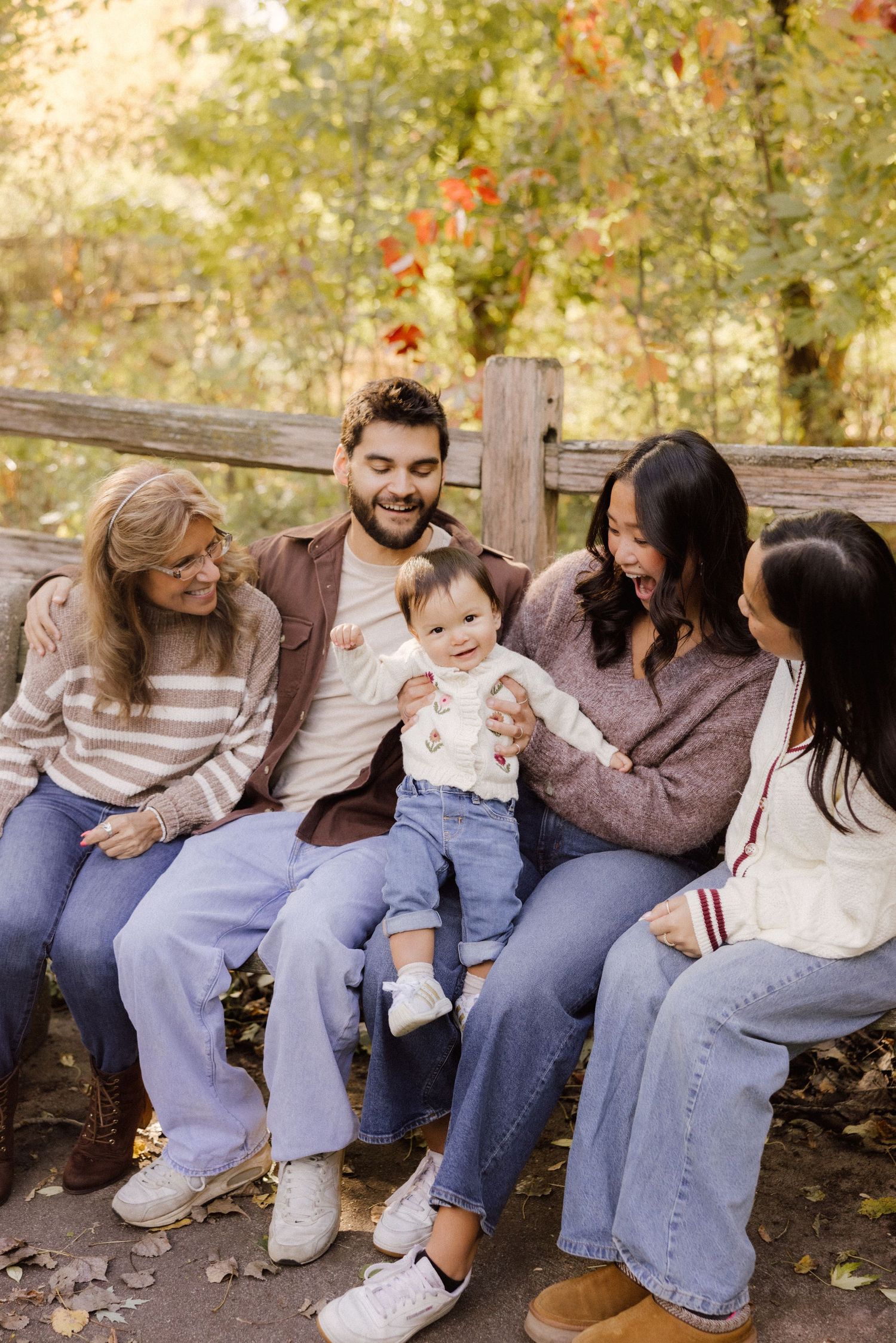 A group sits together on a wooden bench in an autumn setting with fall foliage in the background.