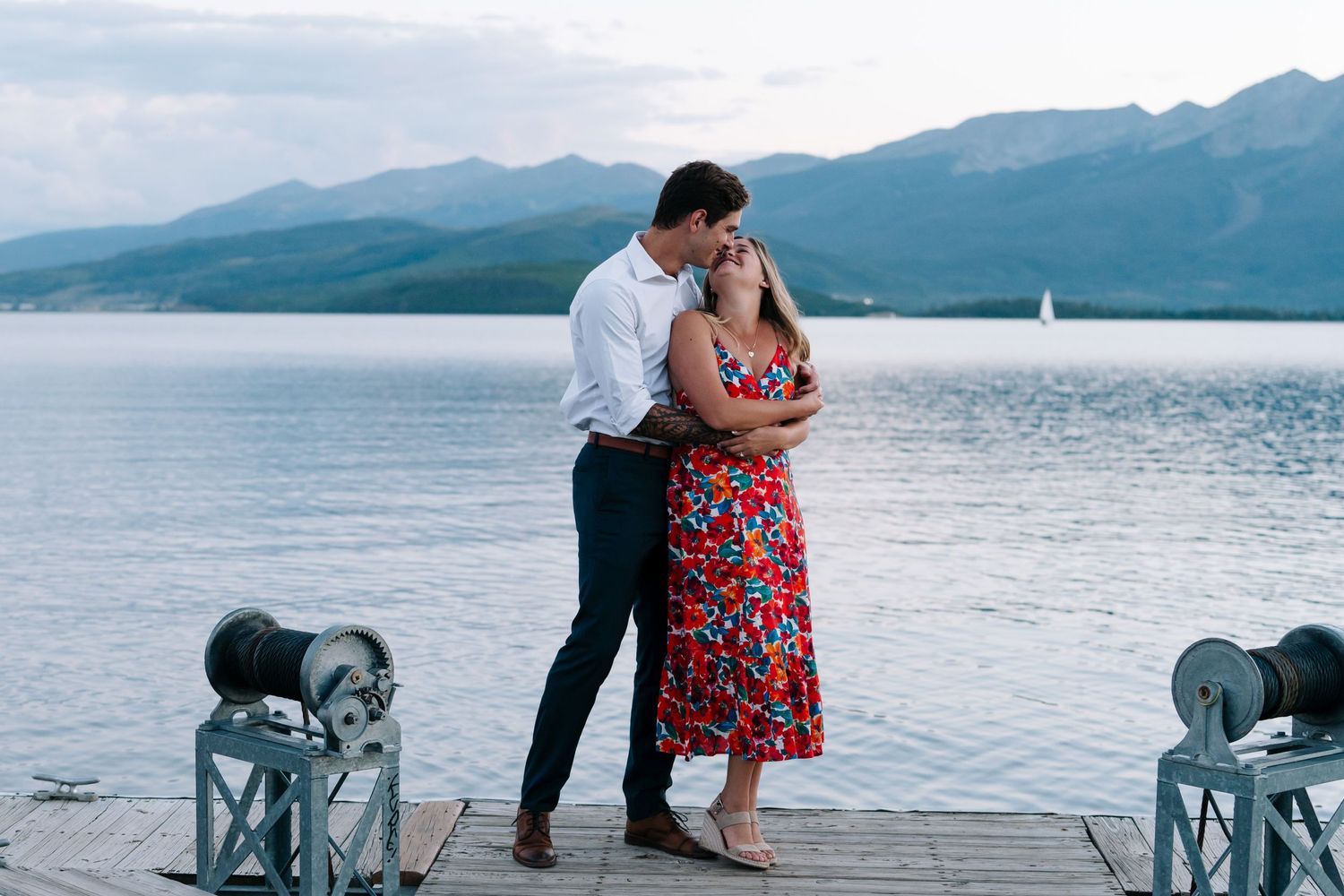 Couple shares a romantic moment on a wooden dock overlooking a scenic mountain lake.