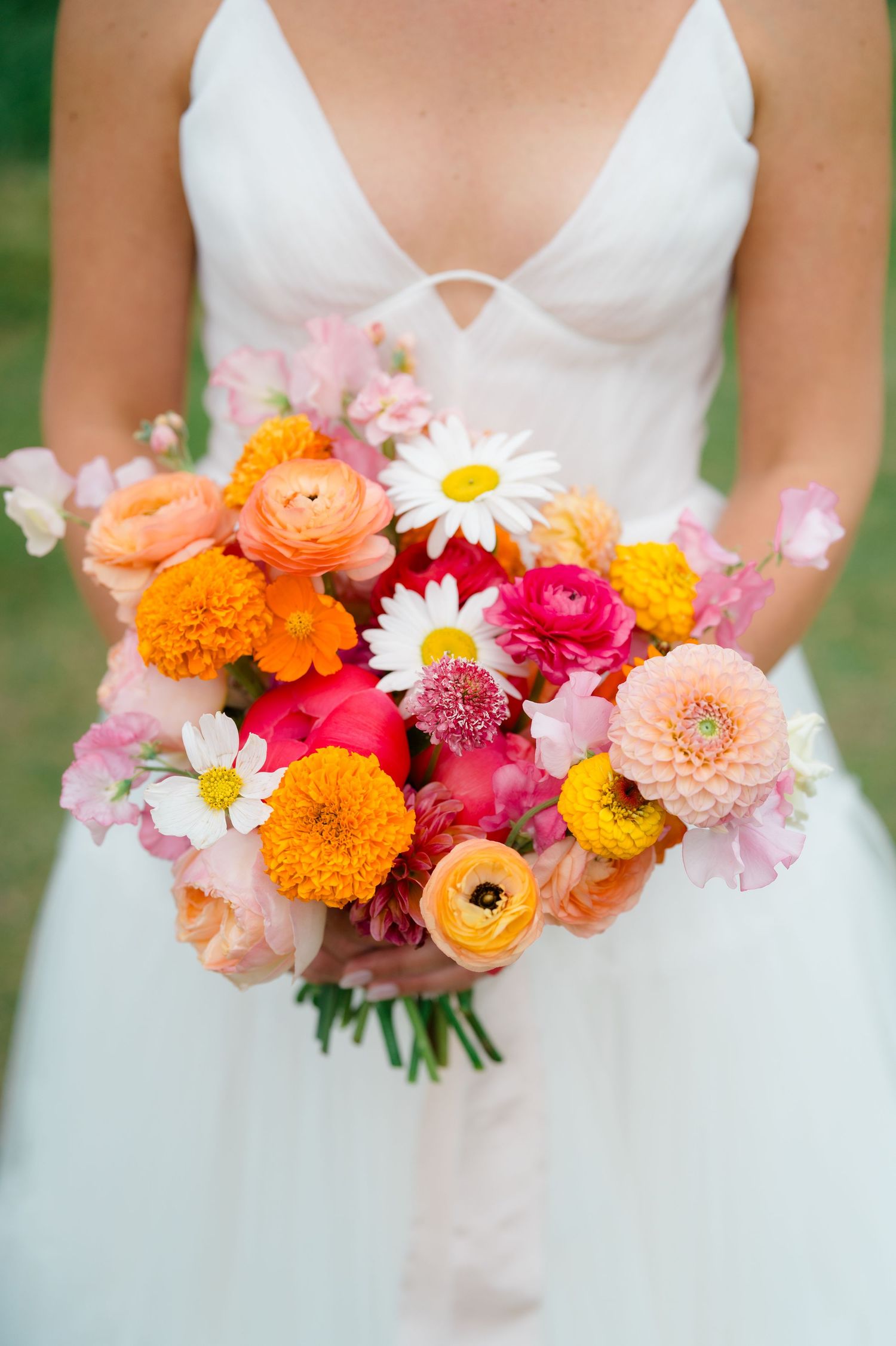 Vibrant summer wedding bouquet featuring orange marigolds, pink dahlias, white daisies and coral ranunculus flowers.