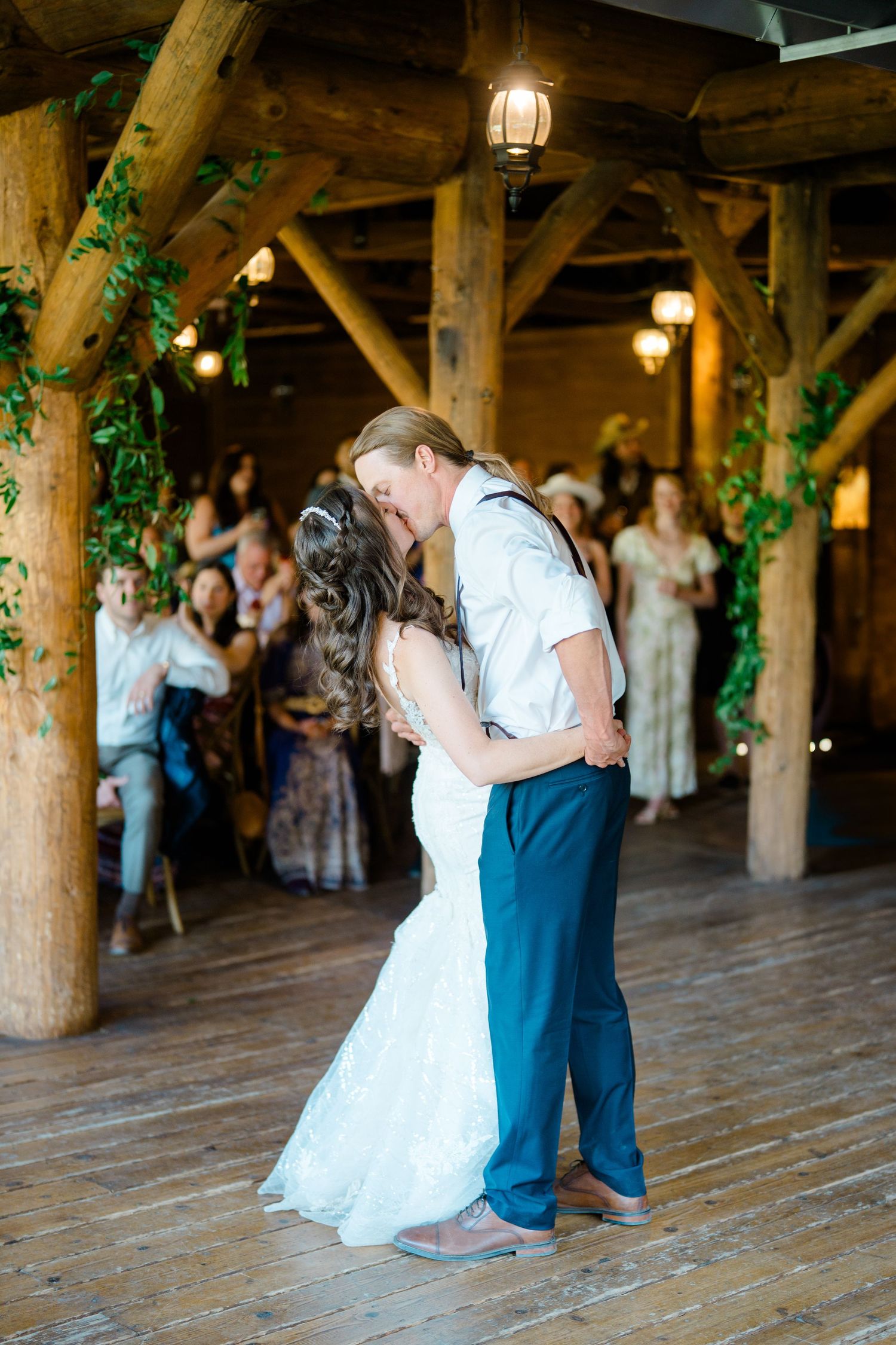 A couple performs their first dance in a rustic wooden barn venue with hanging lanterns at Piney River Ranch.