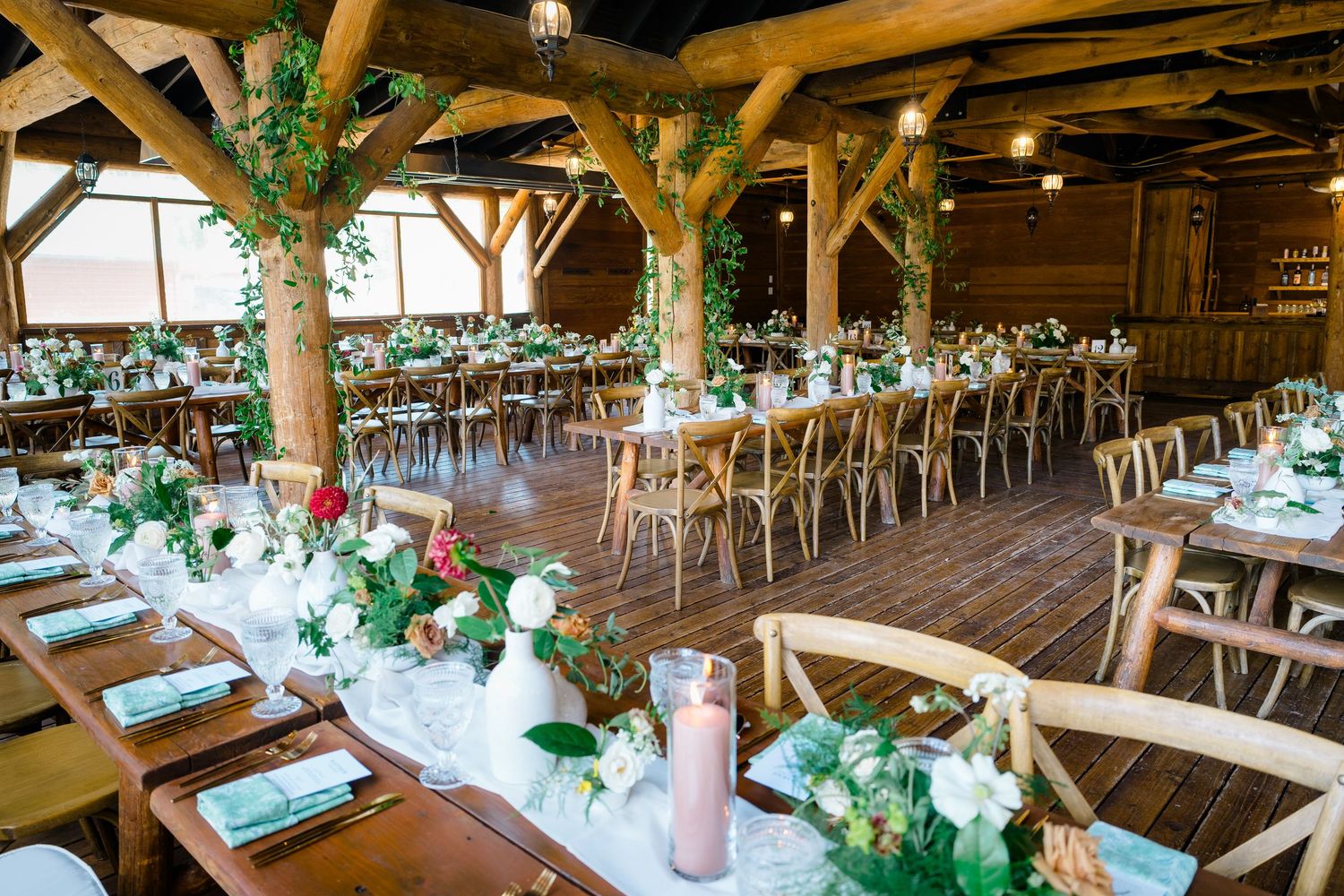 Rustic wooden barn wedding venue with long tables decorated with greenery and white floral centerpieces.