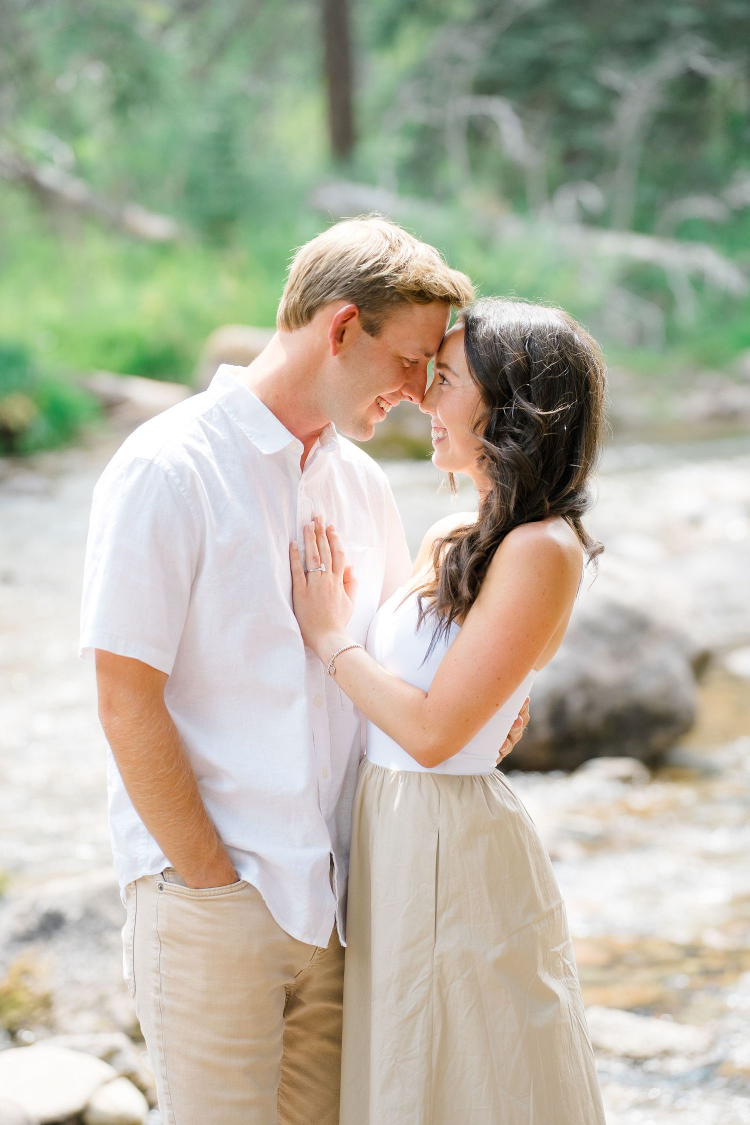 A romantic couple shares tender moments in white and beige outfits against a soft natural outdoor backdrop.
