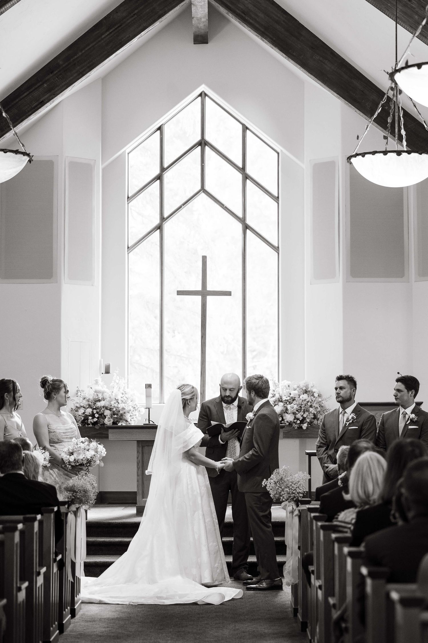 Black and white photo series showing a wedding ceremony inside a bright chapel with large windows and white walls at vail wedding.