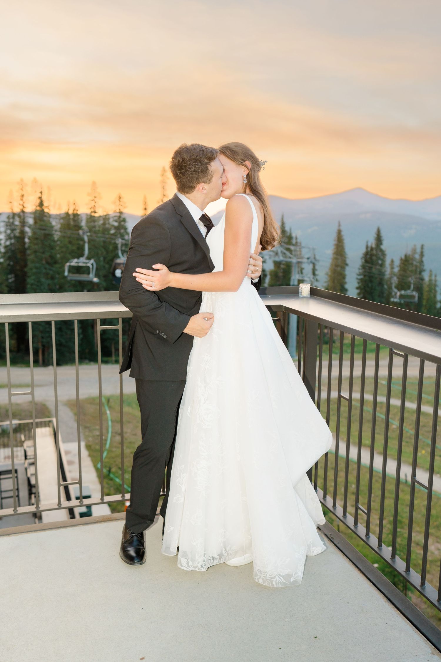 A couple shares a romantic moment on a mountain resort balcony at sunset with ski lifts and evergreen trees in view at copper mountain.