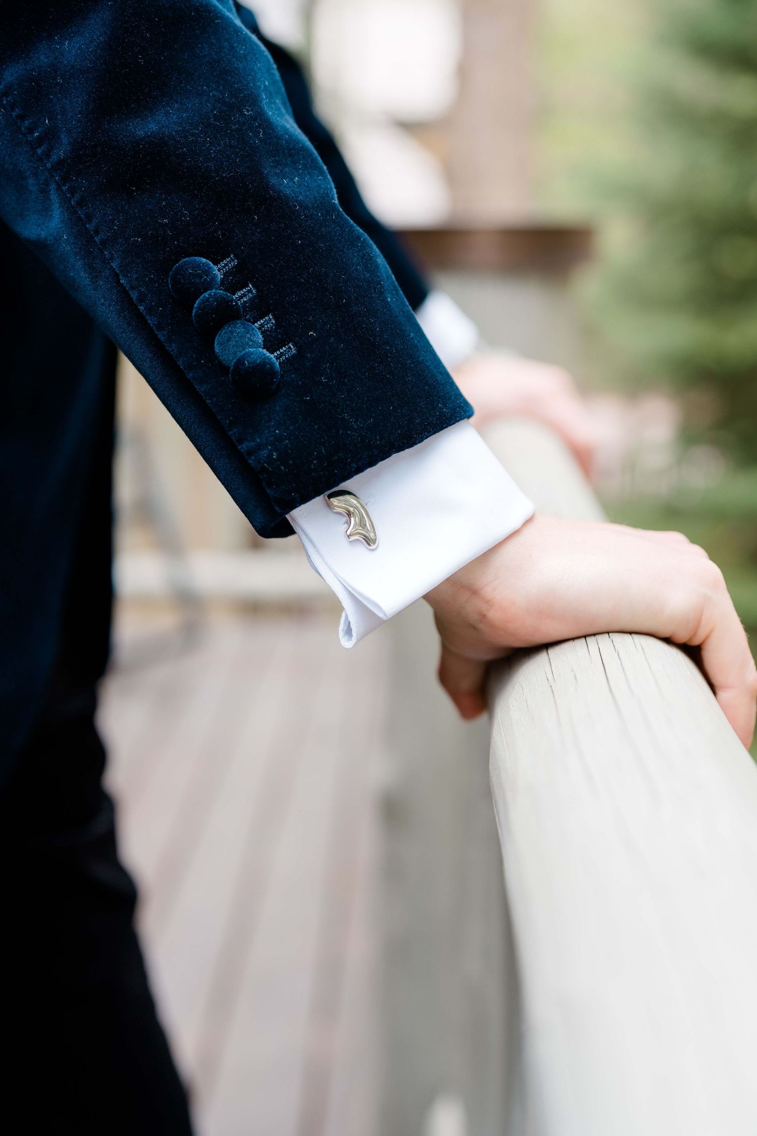 Close-up of a groom's wrist wearing a gold leaf cufflink on a white dress shirt with a navy blue suit jacket at Vail Sonnenalp Wedding.