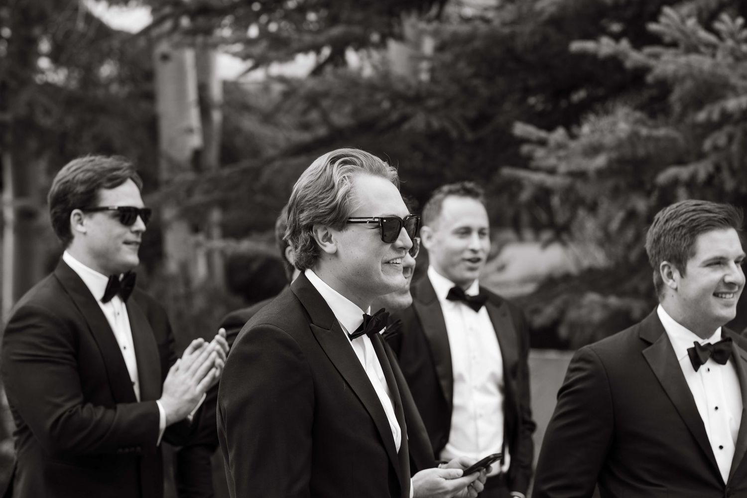 Group of men in black tuxedos and bow ties at an outdoor wedding, black and white photo.