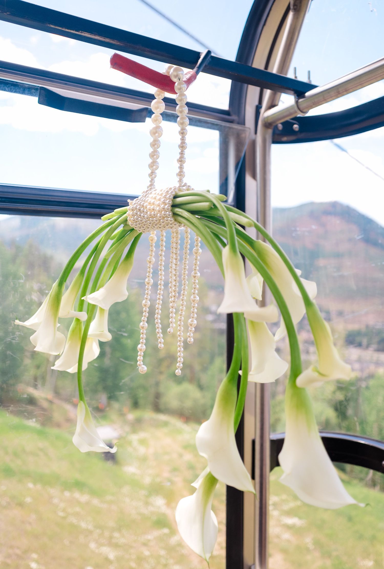Elegant white calla lily hanging bouquet with pearl strands displayed in a gondola with mountain views.