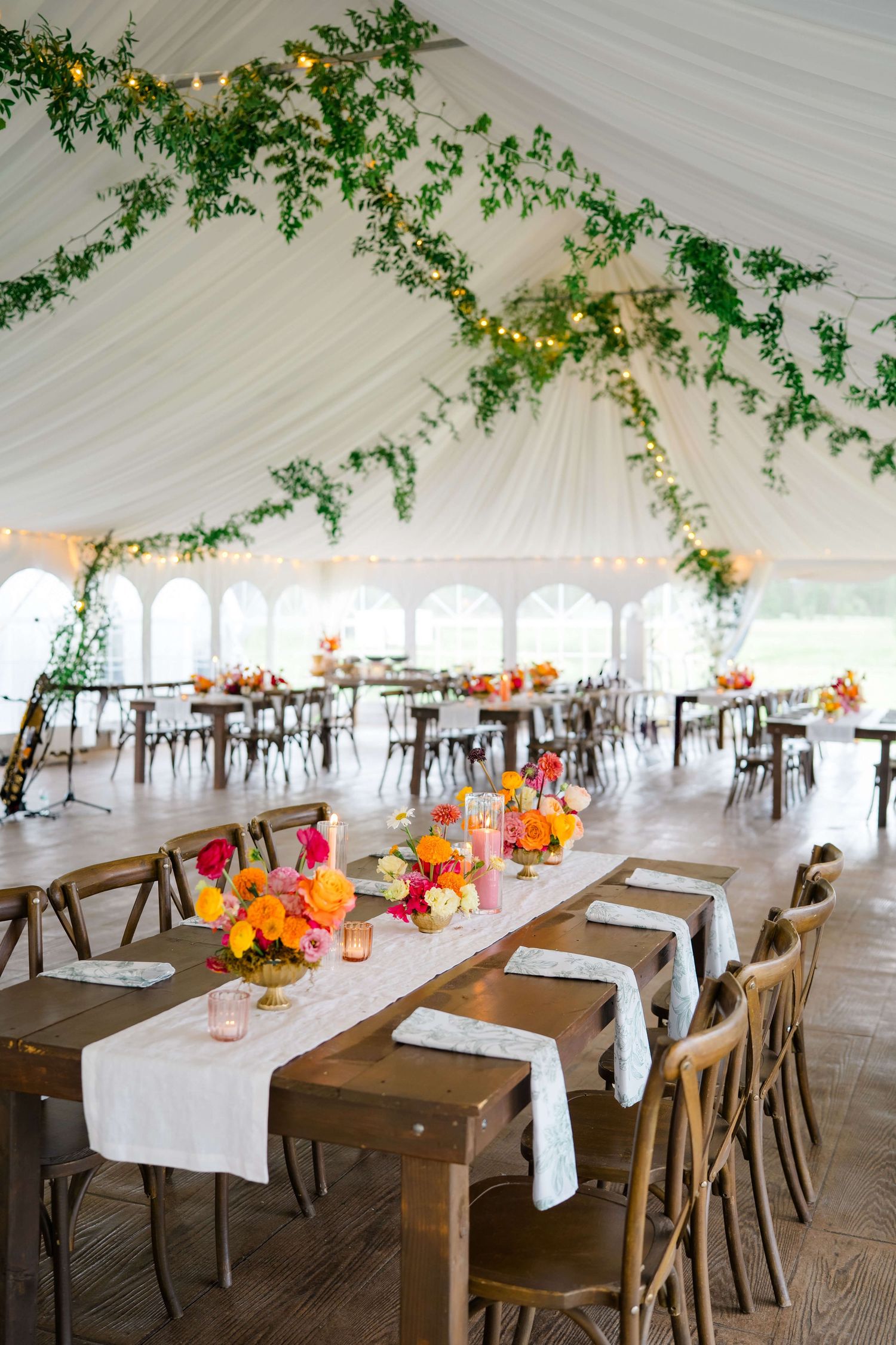 At Camp Hale Wedding Venue - Elegant wedding reception tent with wooden tables, white linens, vibrant floral centerpieces.