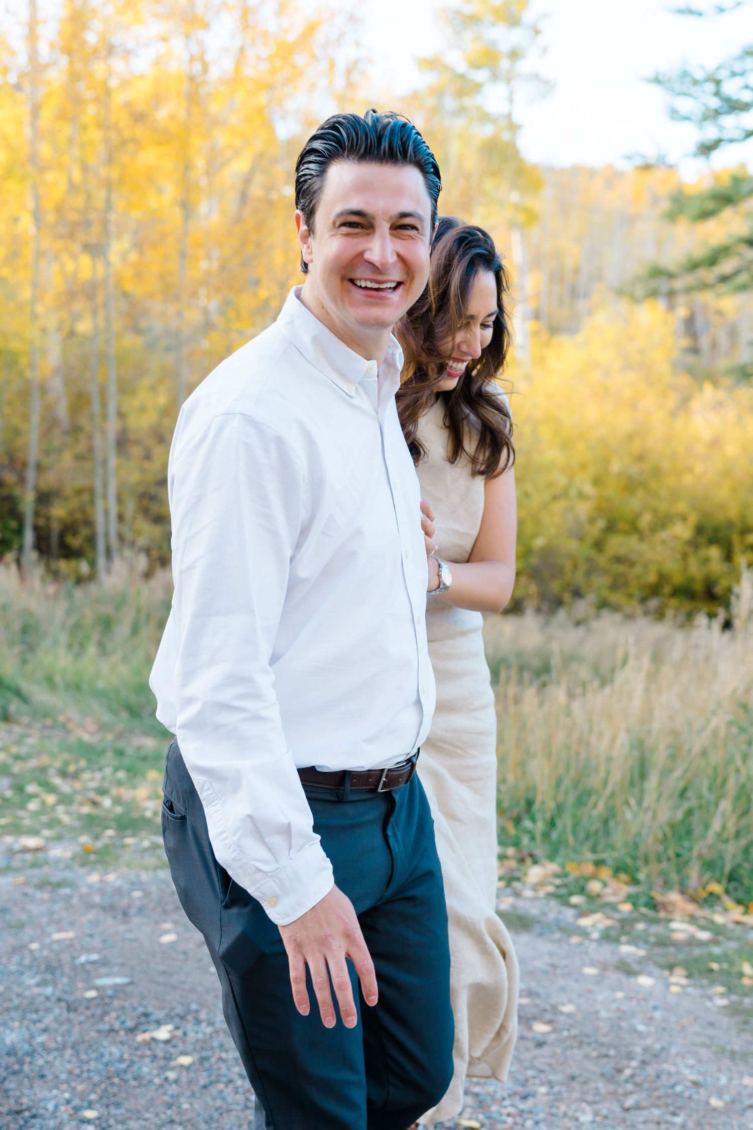 A couple shares a joyful moment together outdoors surrounded by golden autumn trees and foliage.