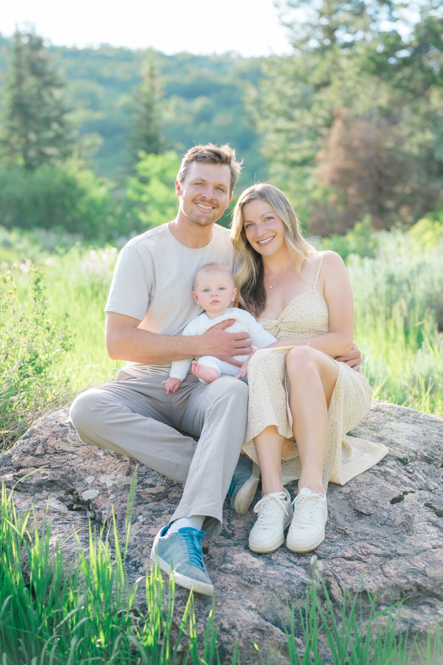 A family sits together on a rocky outcrop surrounded by mountain greenery.