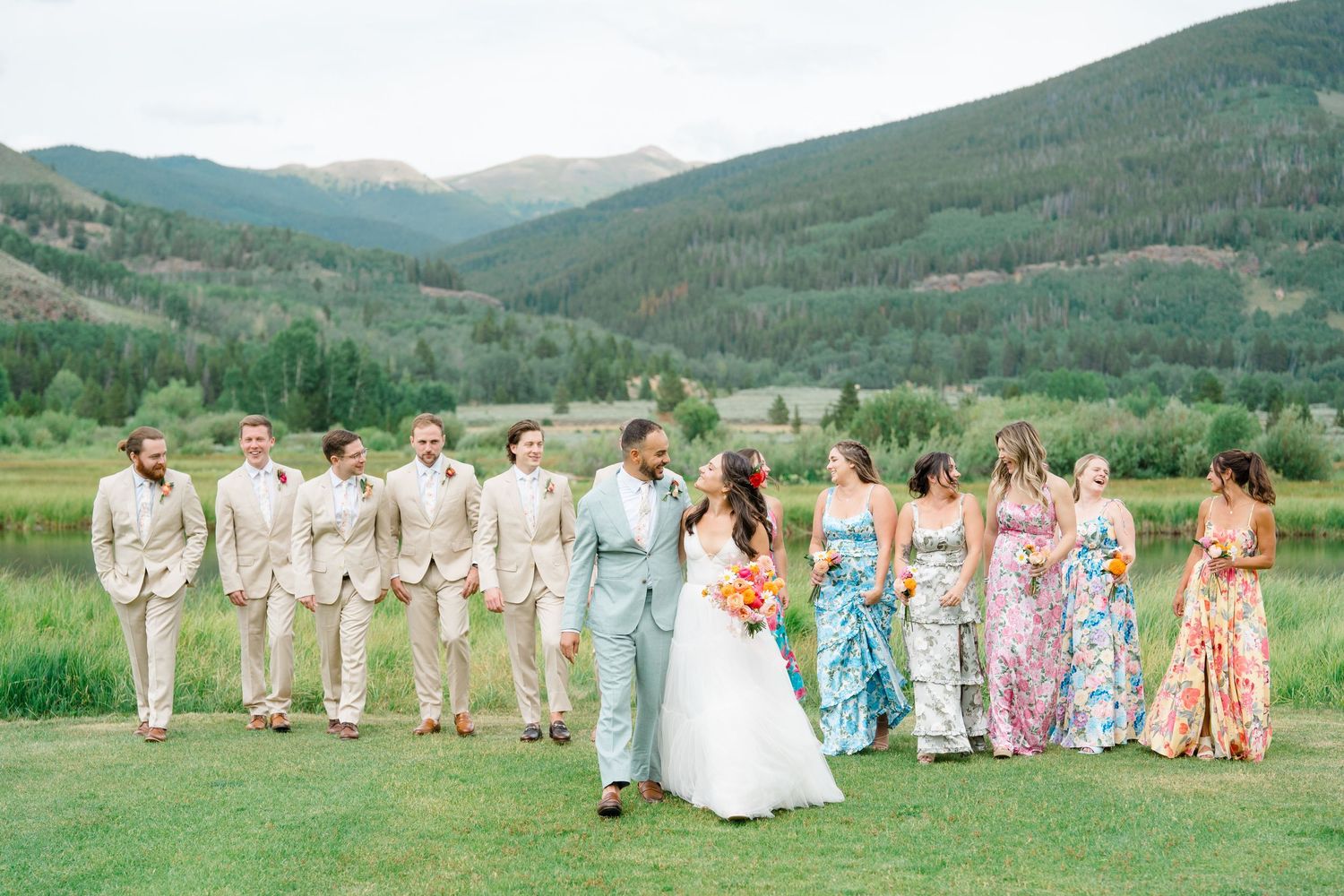 Wedding party poses in front of scenic mountain landscape with lush green forests and rolling hills.
