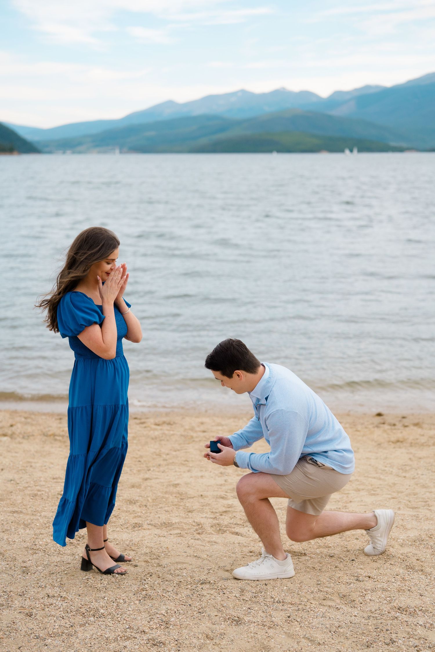 A couple on a beach with mountains in the background during a surprise proposal moment at lake dillon marina.