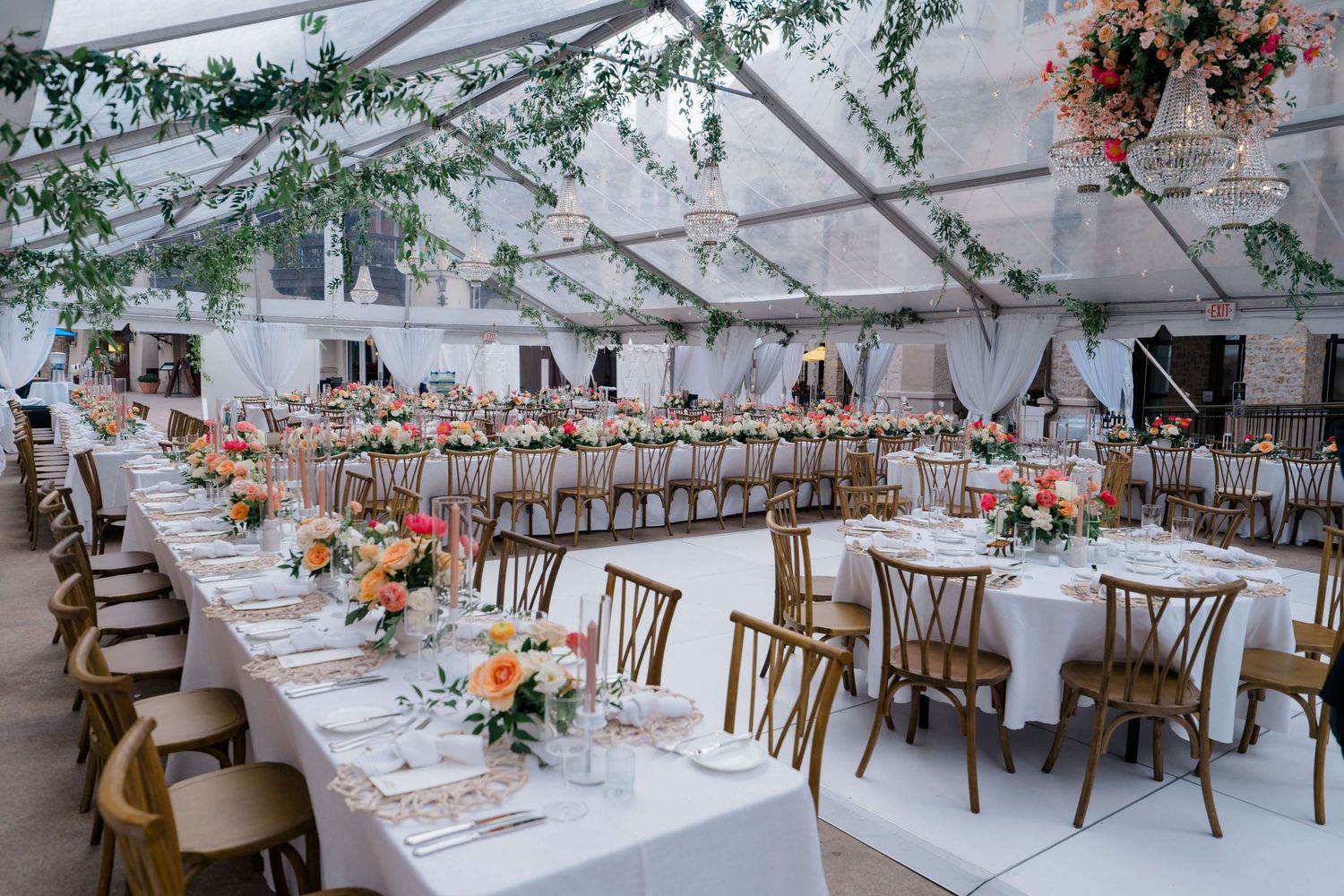Elegant wedding reception under a clear tent with long white tables, floral centerpieces, and wooden cross-back chairs at Arrabelle in Vail.