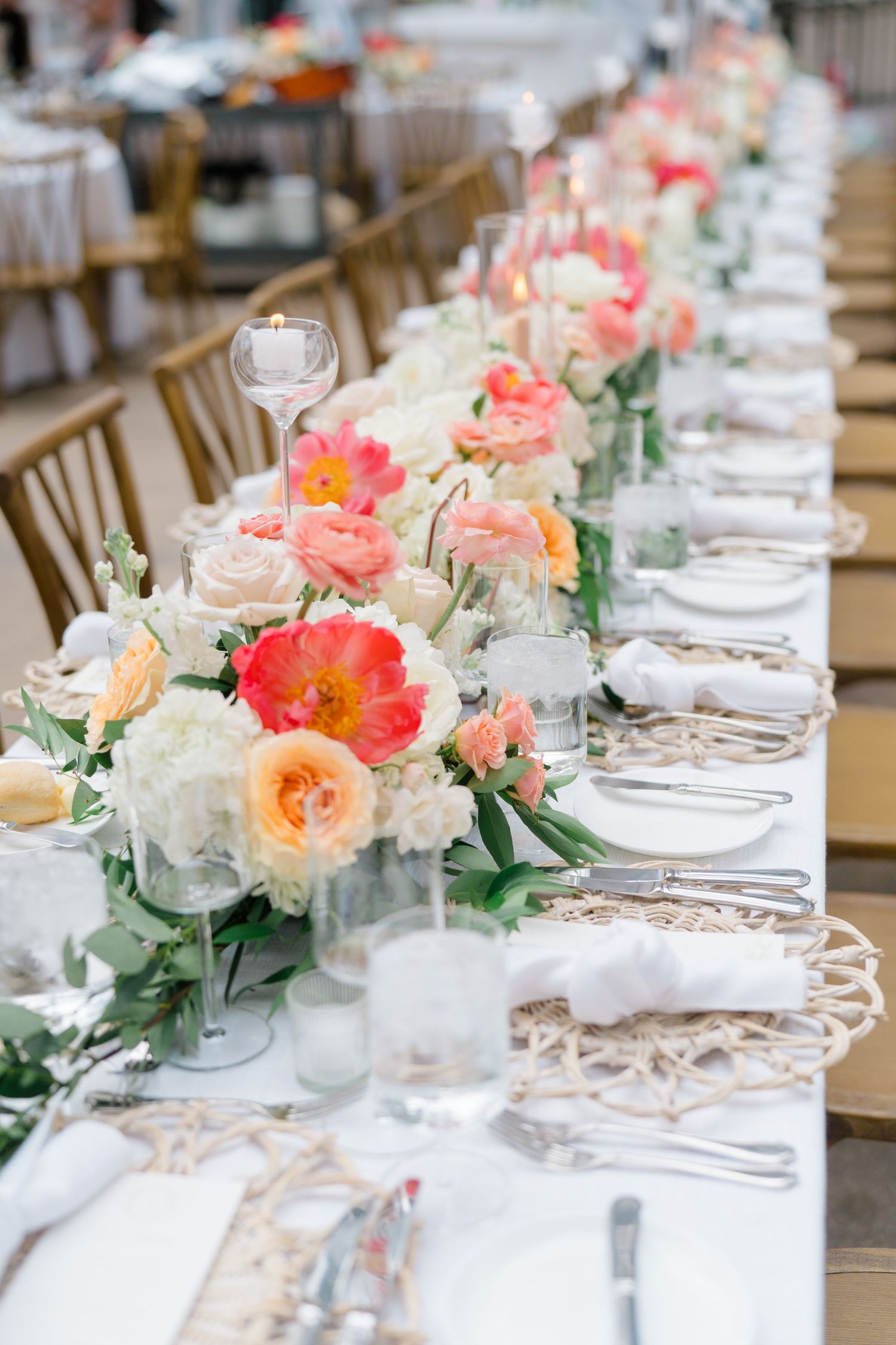 At Arrabelle Vail Wedding, wedding reception table with coral, peach, and white floral centerpieces, candles, and woven charger plate.