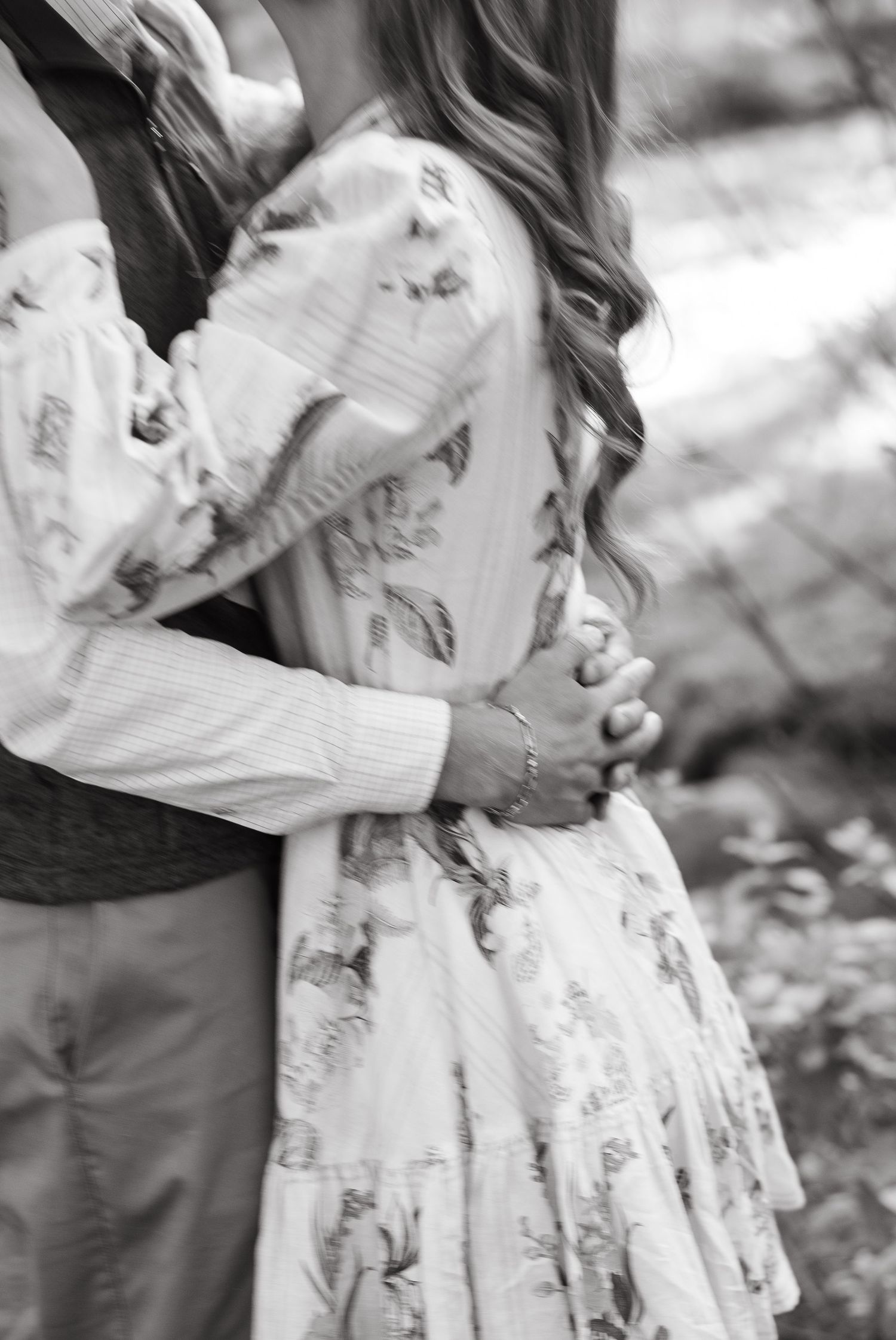 Black and white photo of a couple embracing, woman in floral dress with long wavy hair, man in striped shirt.
