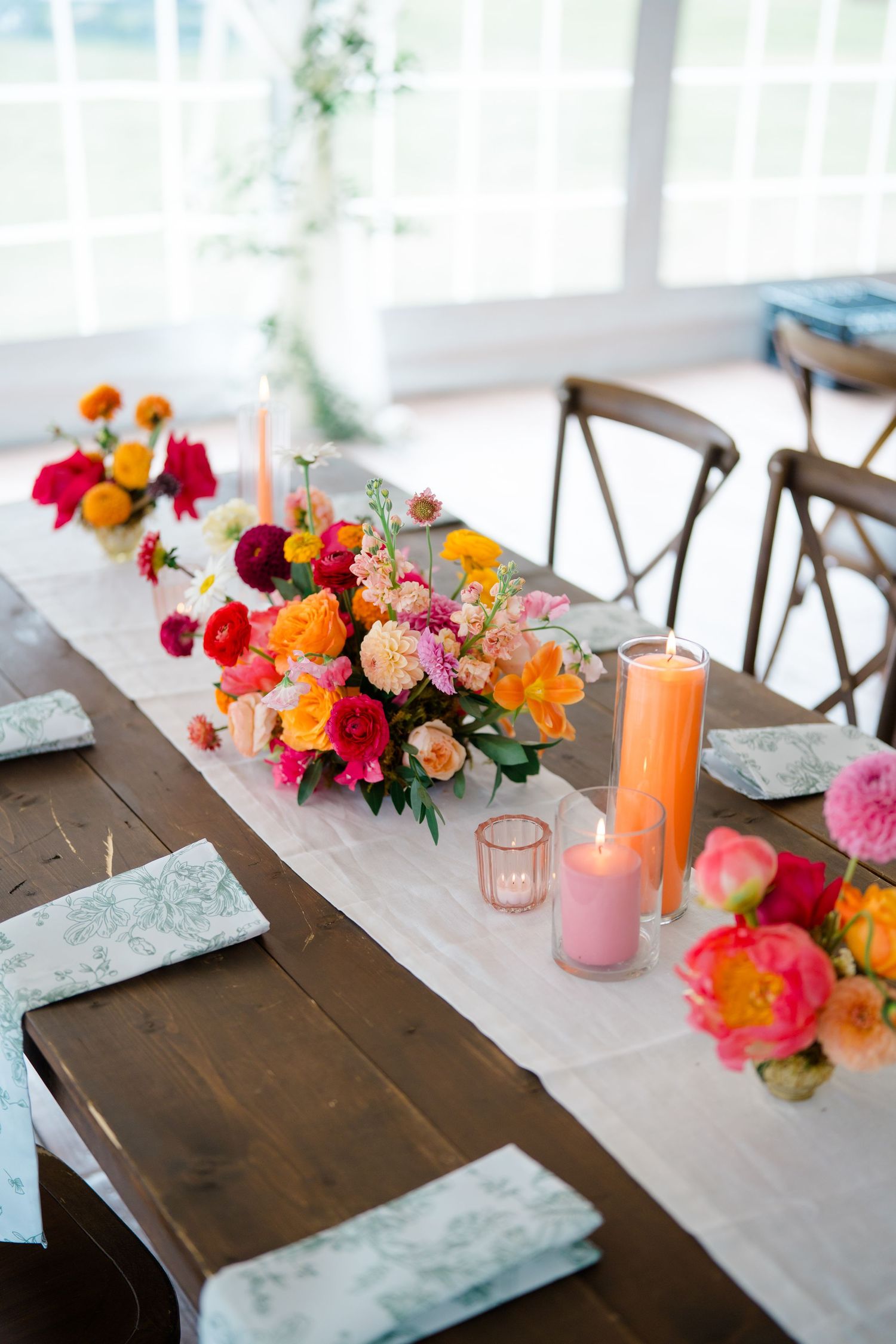 Rustic wooden table decorated with colorful floral arrangements and pink and orange candles.