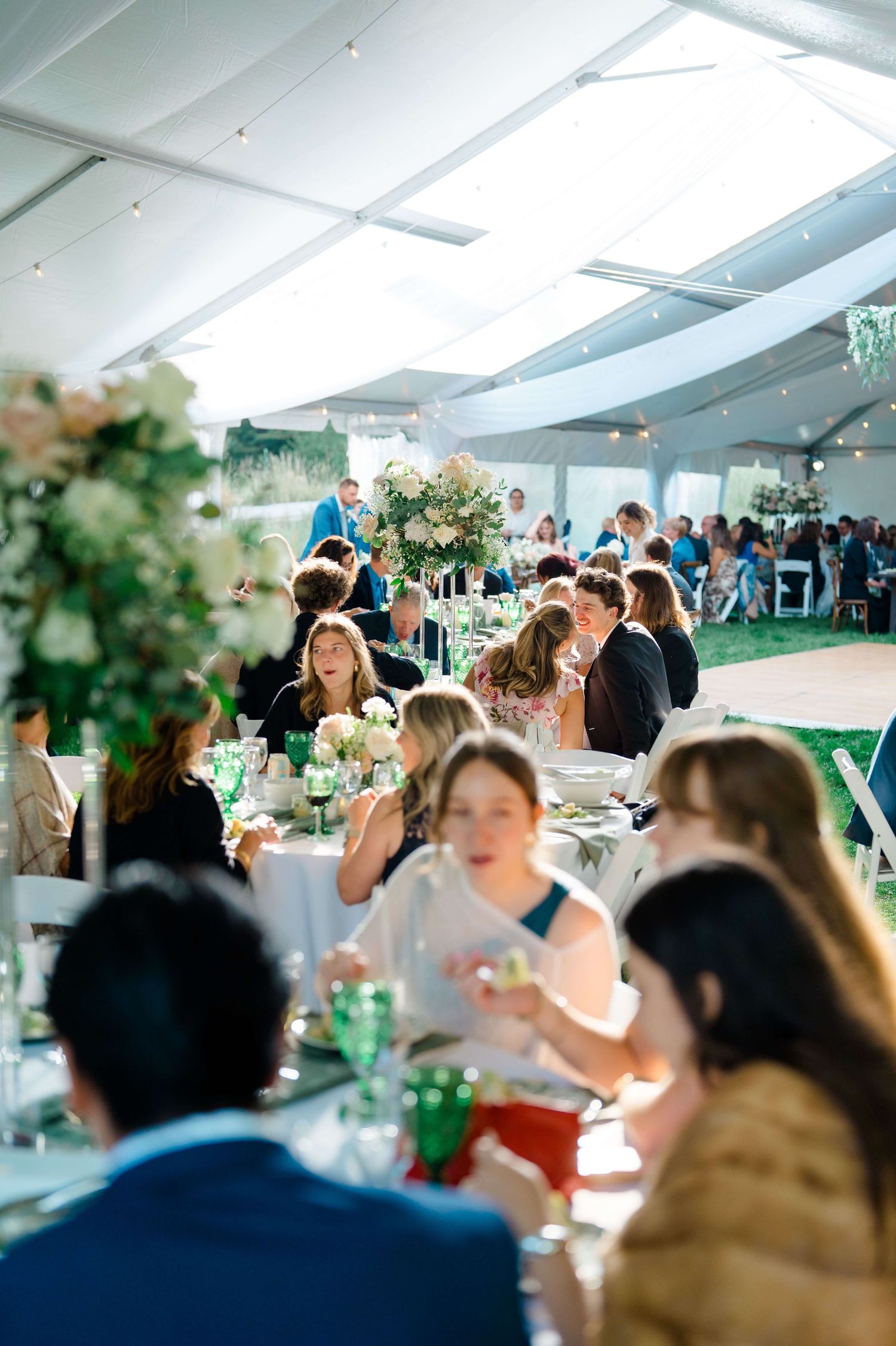 Wedding guests enjoy a reception dinner under a white tent with elegant table settings and greenery decor at vail tented wedding.