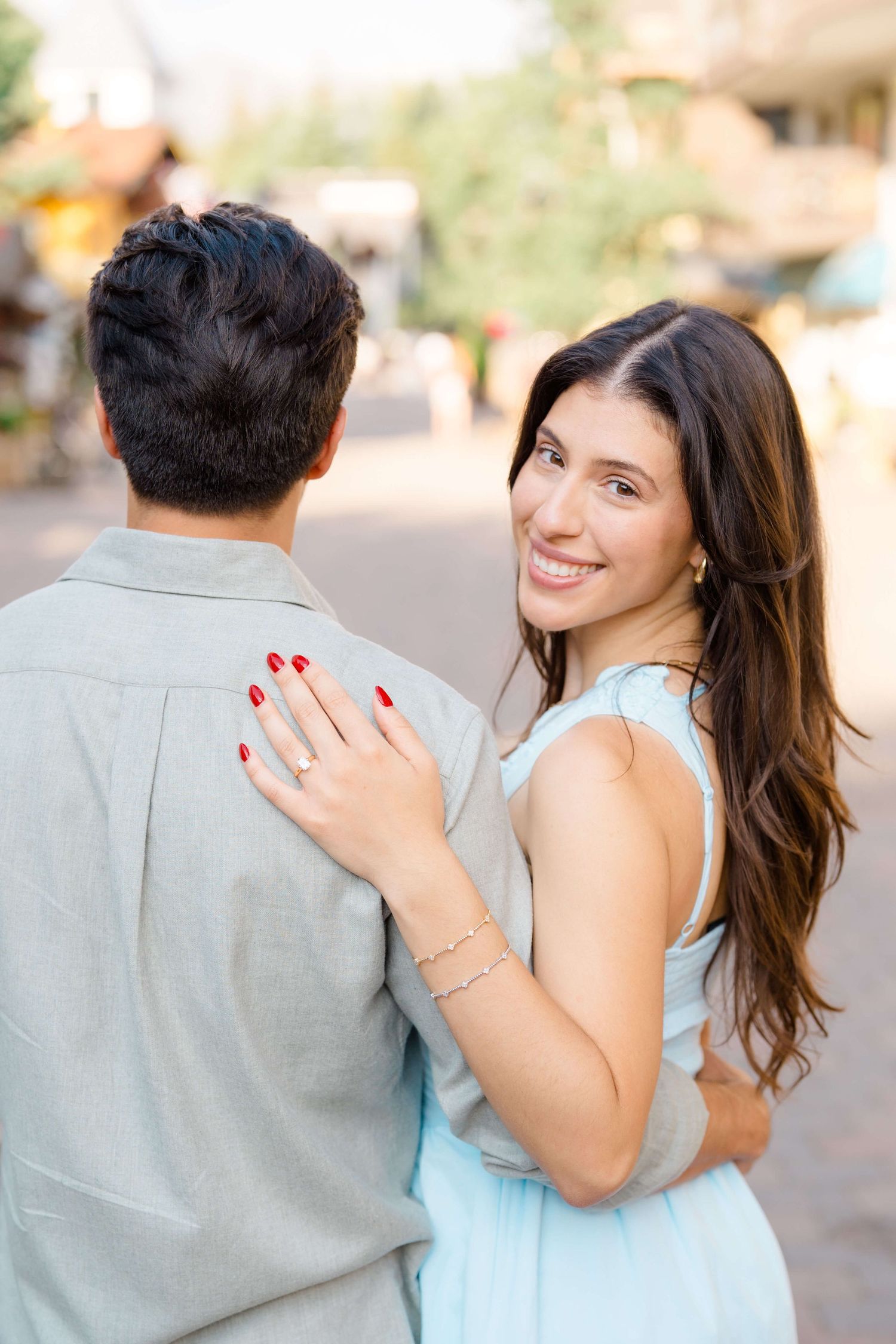 A couple in a light blue dress and grey shirt embrace during an outdoor engagement photo session following vail village proposal