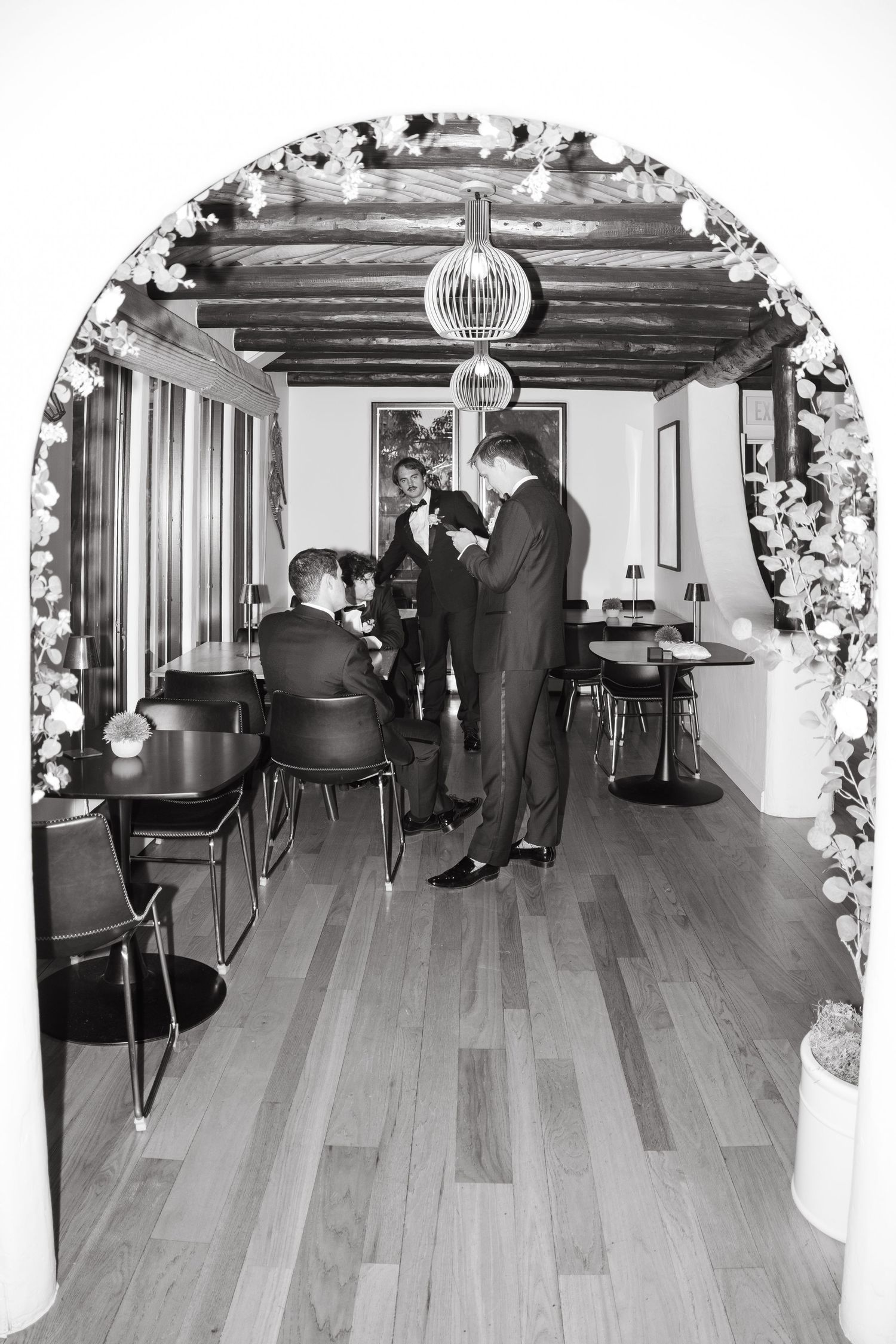Black and white photo of an empty wedding venue with floral decorations and hardwood floors.