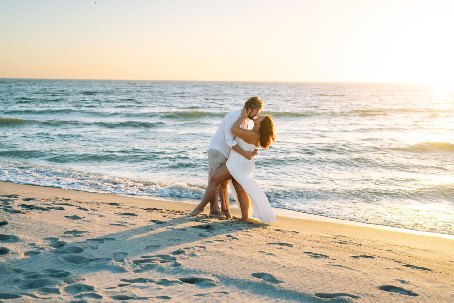 couple embrace as they are about to kiss on the beach next to the water